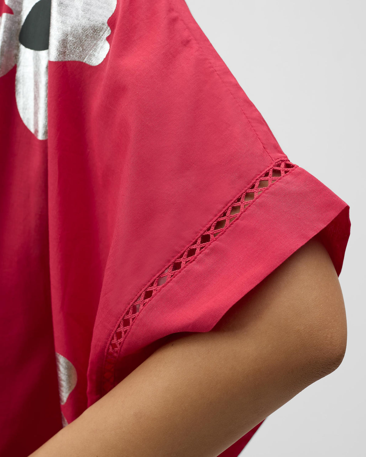 Close-up of ladder lace and a silver foil flower on a watermelon pink top.