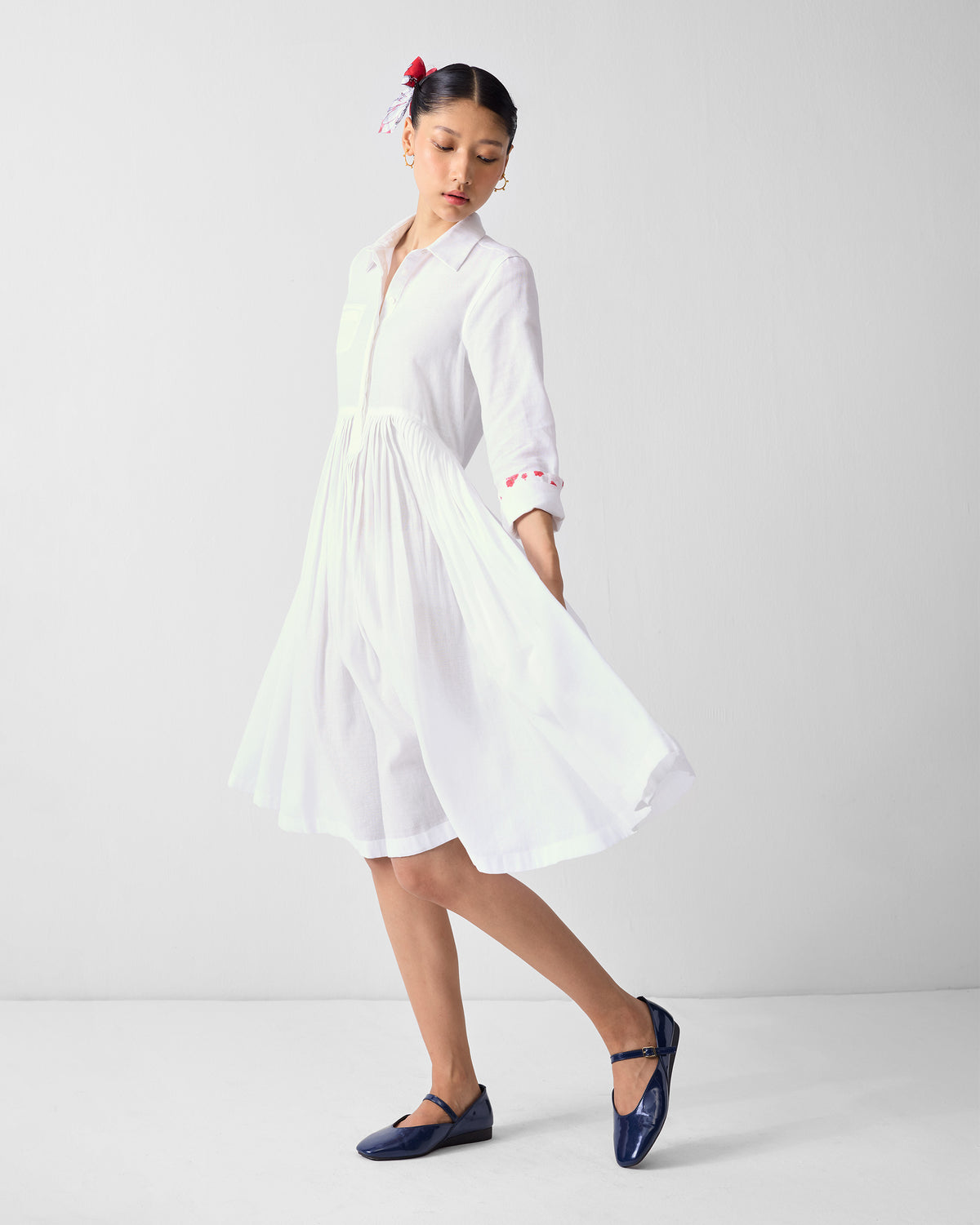 Three-quarter view of a white shirt dress with a flared pleated skirt.