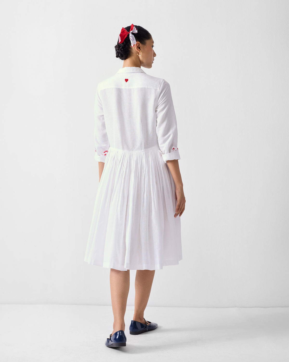 Back of a white shirt dress with a red heart and a pleated skirt.
