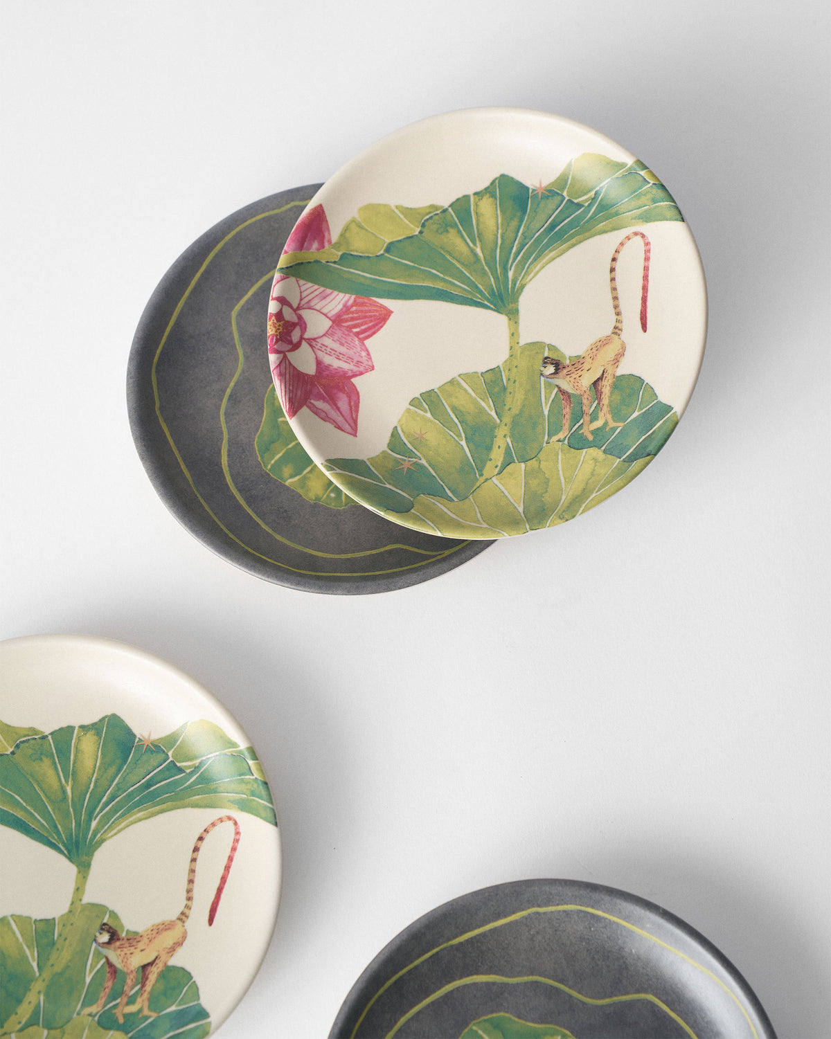 Float tea plates overlapping in cream monkey and charcoal designs.