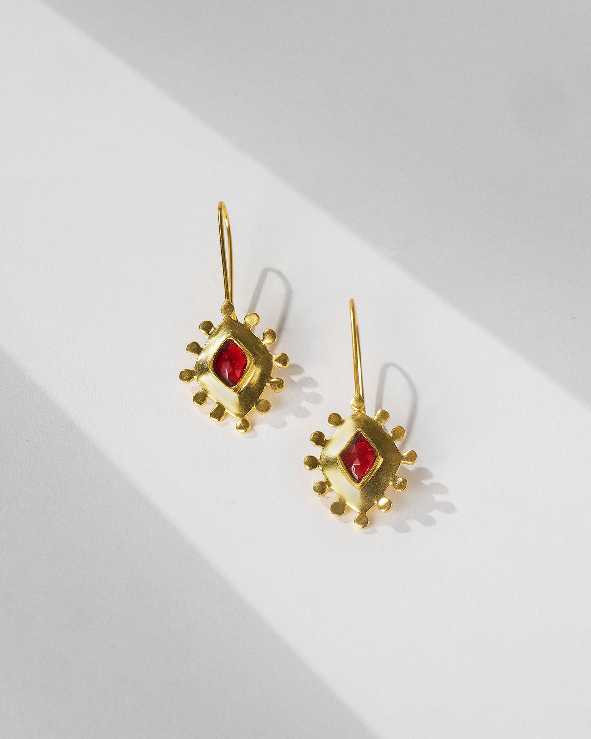 Pair of gold garnet barfi drops with red glass laid flat.
