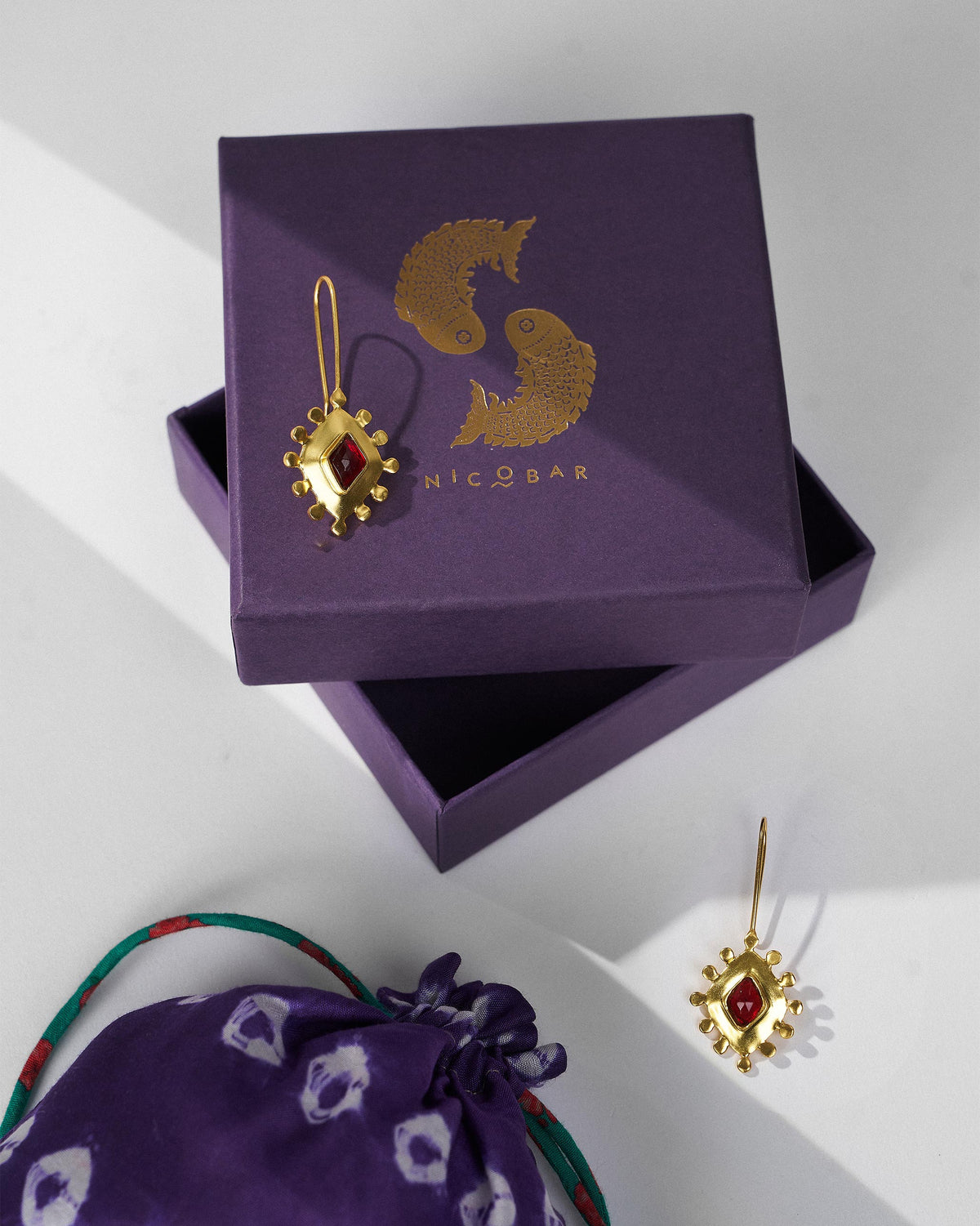 Gold garnet barfi drops on a purple Nicobar gift box.