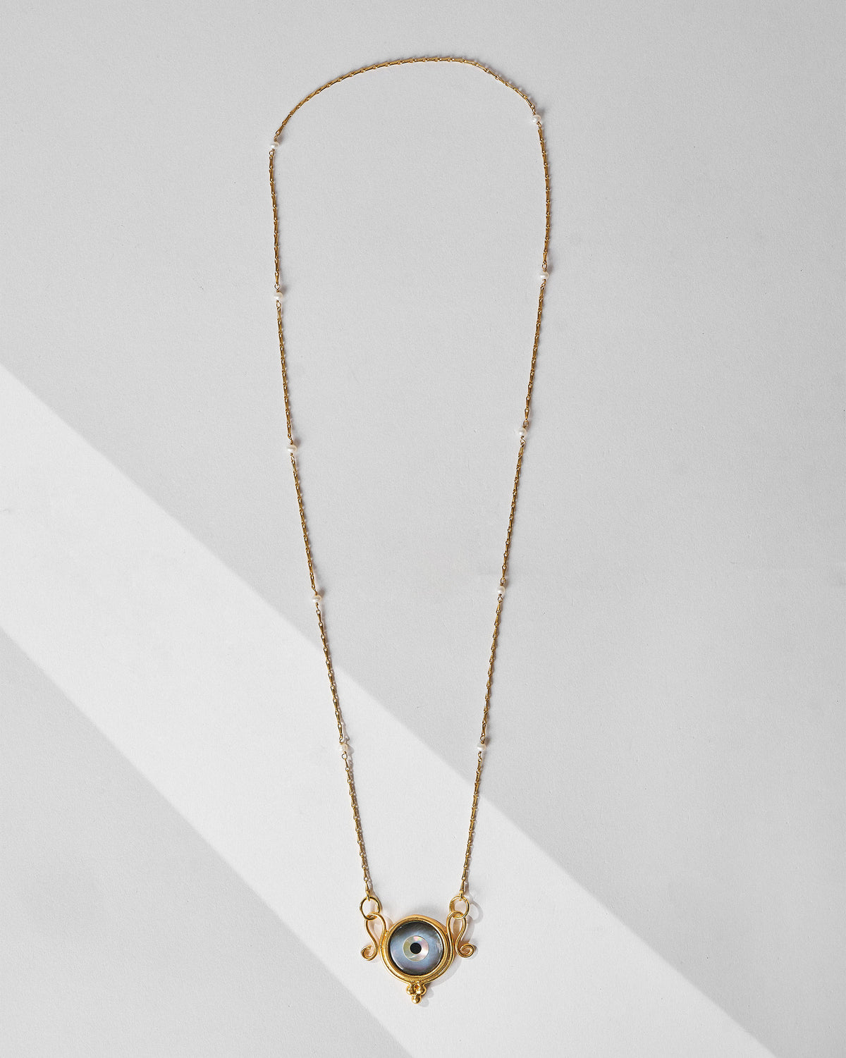 Gold Turki Nazar chain laid flat with an eye pendant and pearl beads.