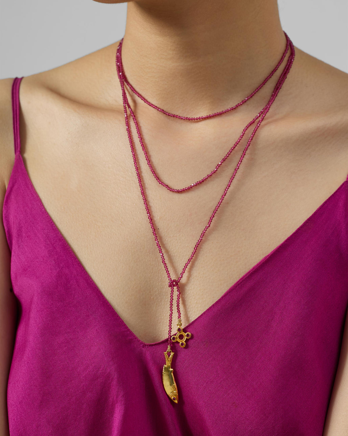 Person wearing a layered Jal Pari magenta bead necklace with gold fish and flower charms.