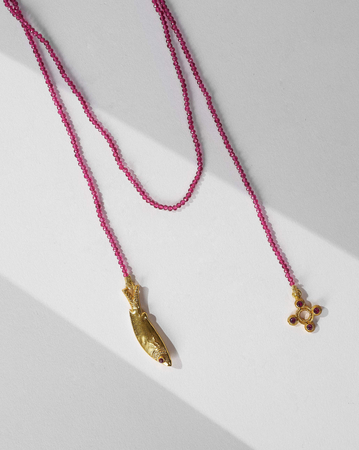 Jal Pari magenta bead necklace with a gold fish charm and a four-lobed charm.