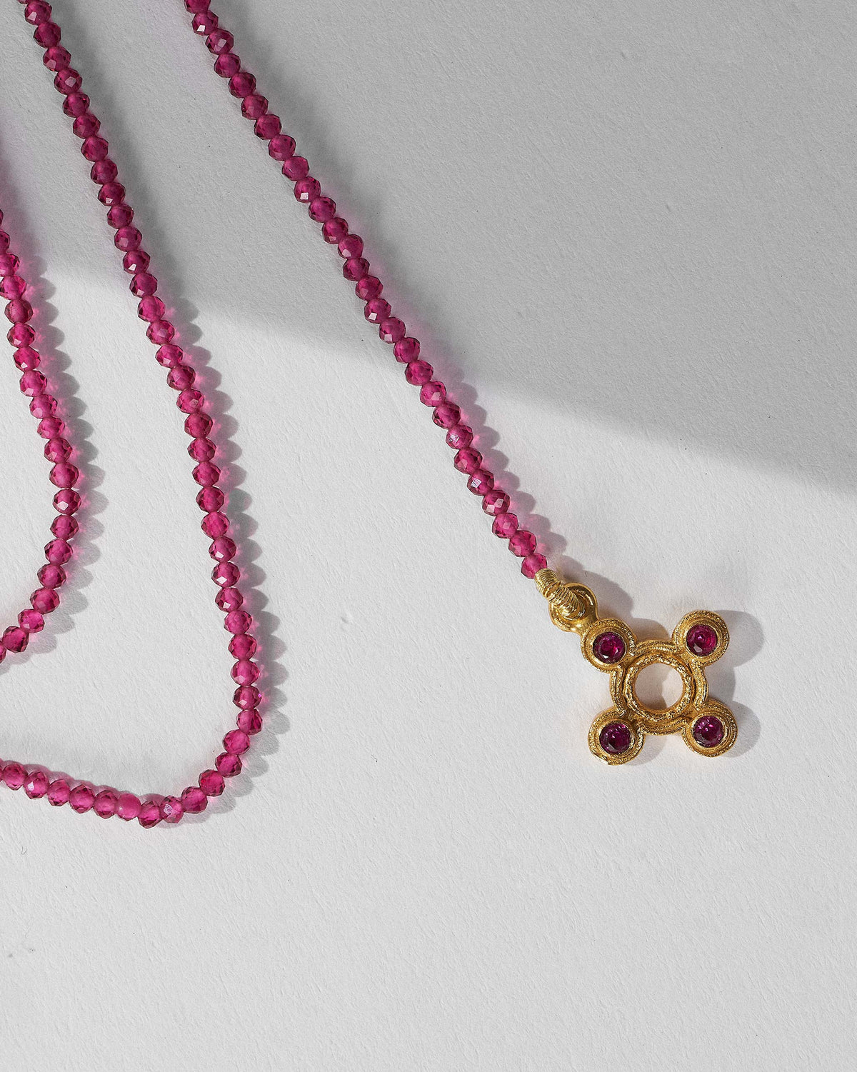 Close-up of the gold four-lobed charm on a Jal Pari magenta bead necklace.