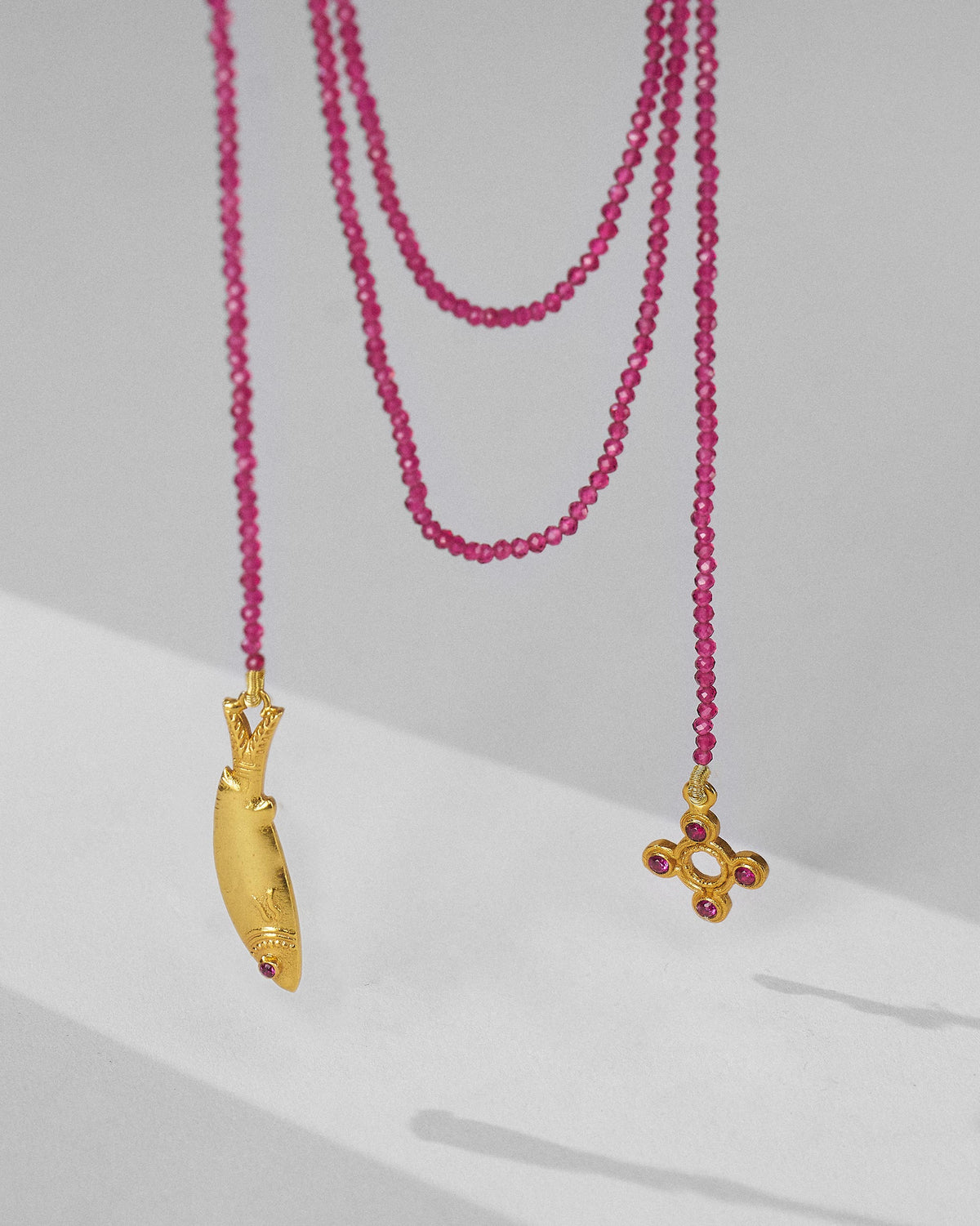 Jal Pari magenta bead necklace hanging with gold fish and flower charms.