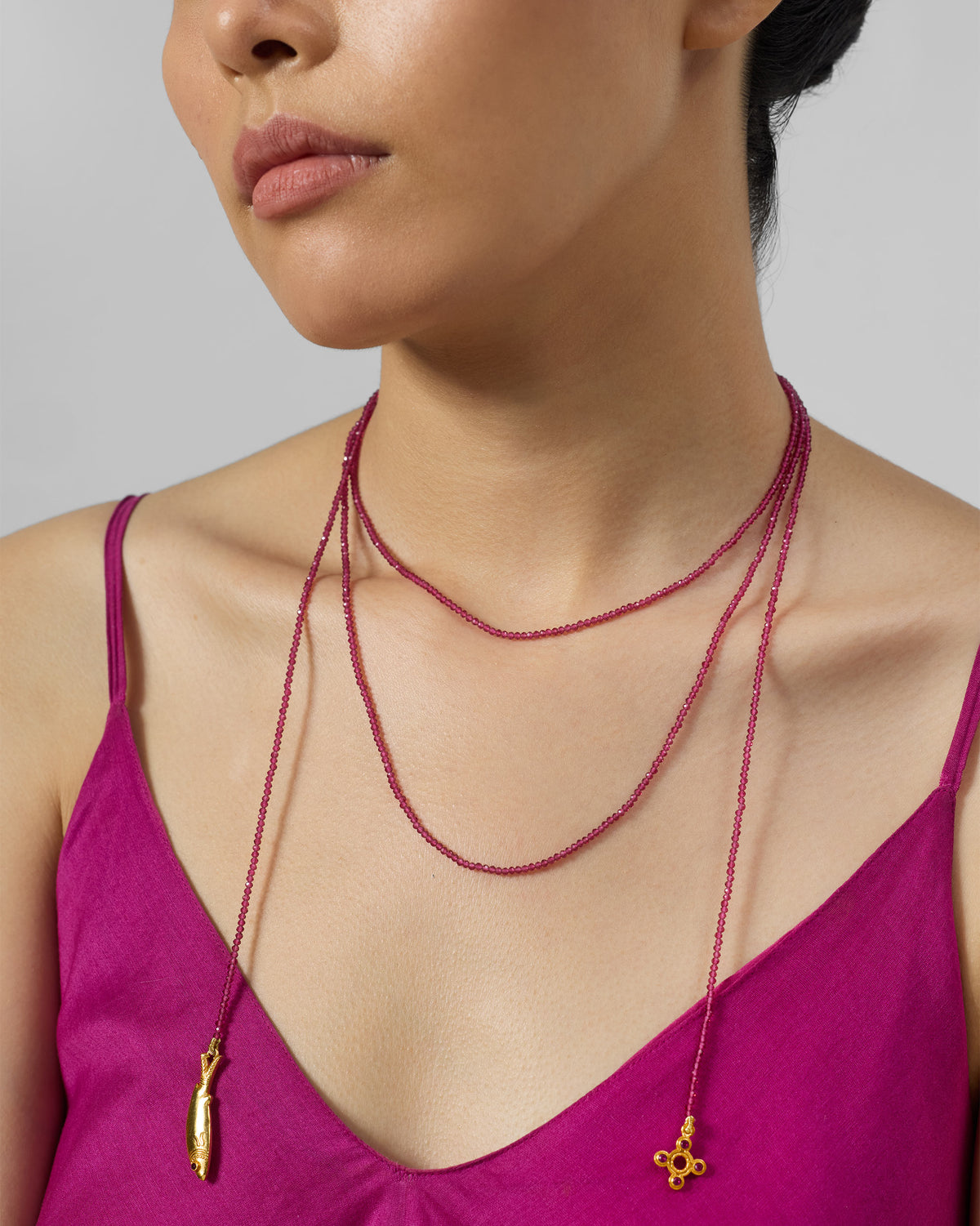 Close-up of a layered Jal Pari magenta bead necklace with gold charms.