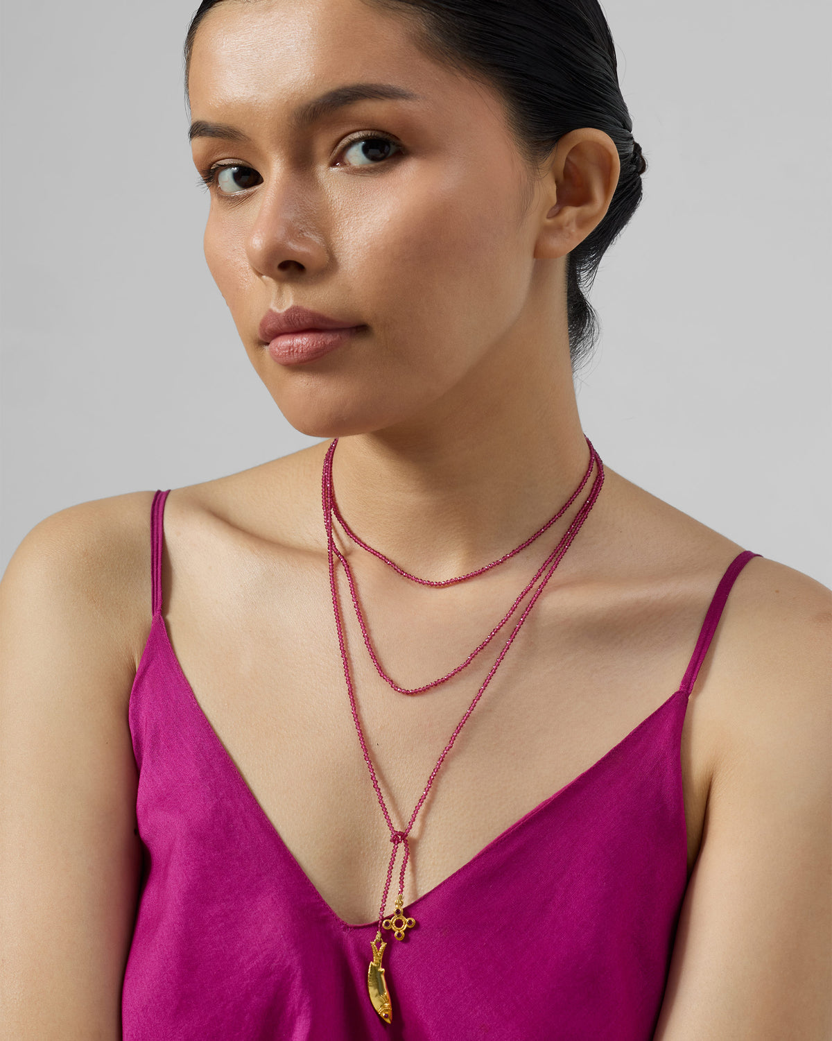 Person wearing a wrapped Jal Pari magenta bead necklace with gold charms.