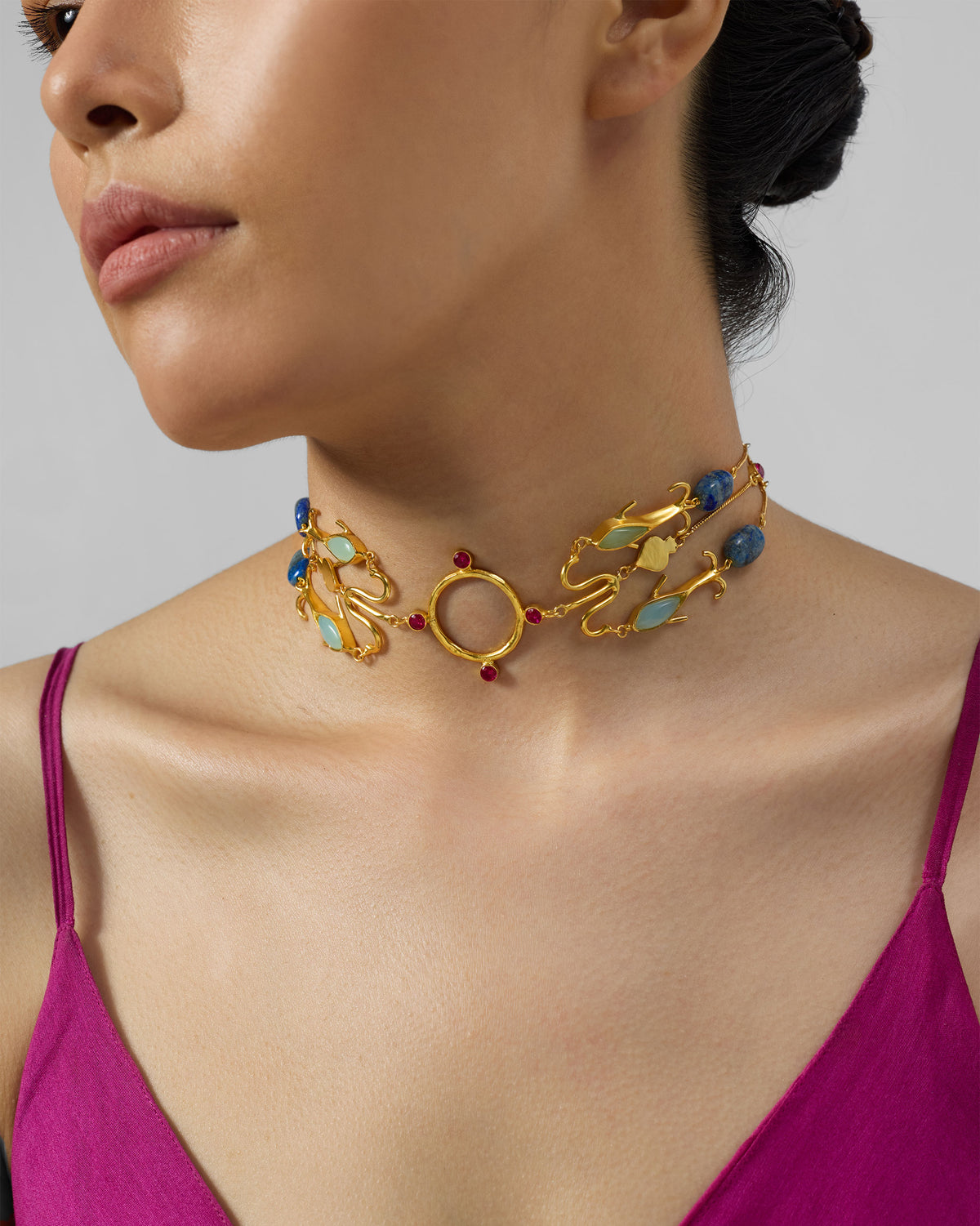 Gold Indus necklace with fish motifs, a central ring, and blue and red stones.