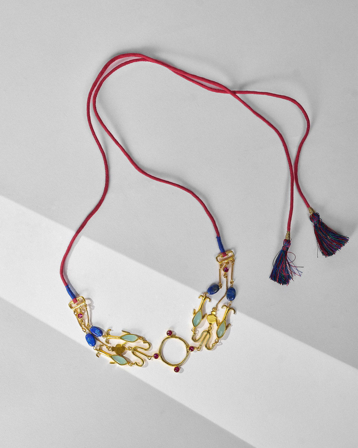 Gold Indus necklace on a red cord with blue tassels and mixed stone inlays.
