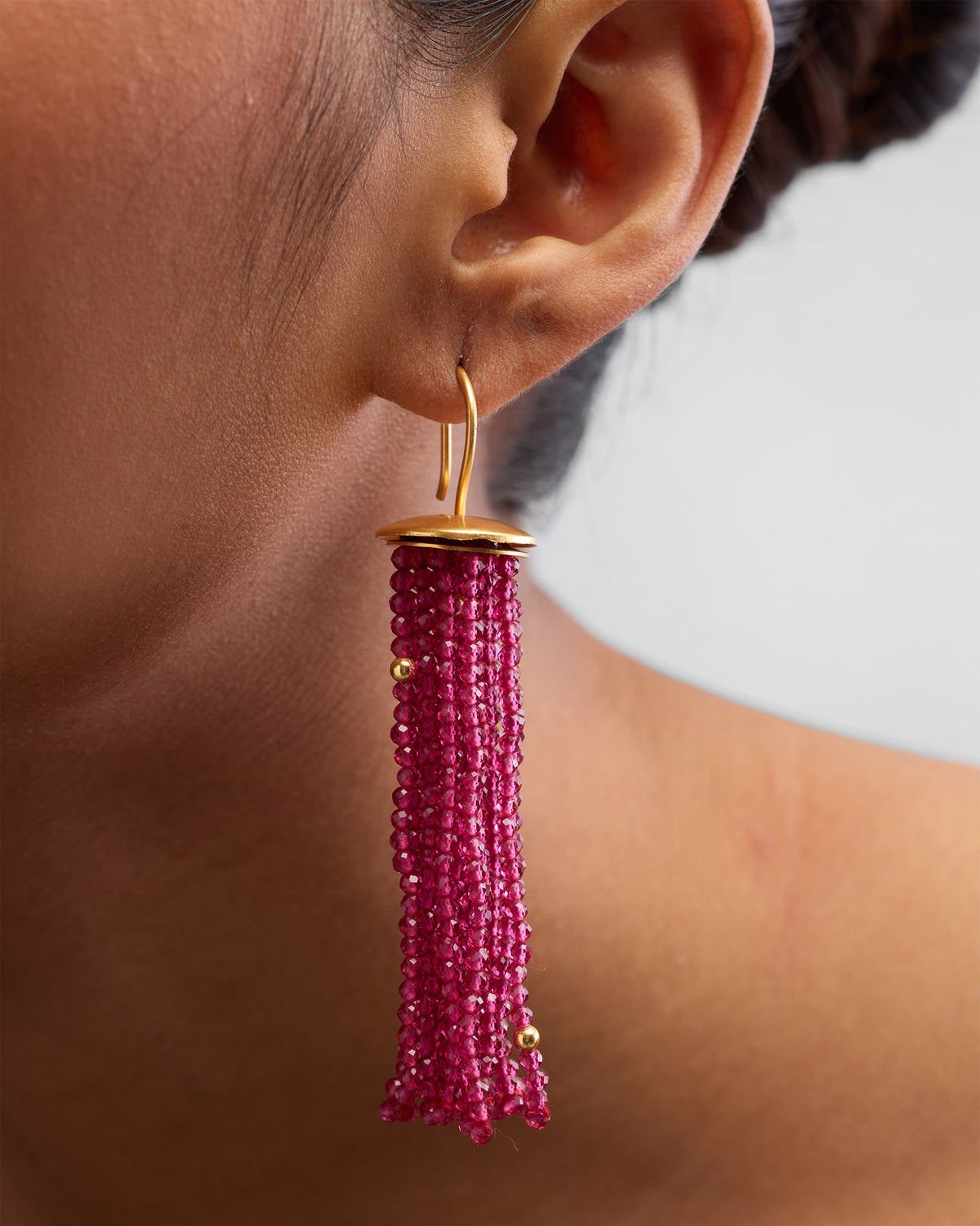 Side profile of a magenta Glass Tassel earring with gold hardware on a person.