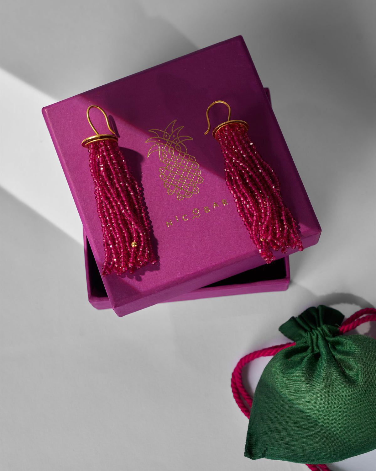 Magenta Glass Tassel earrings on a magenta Nicobar box with a green pouch.