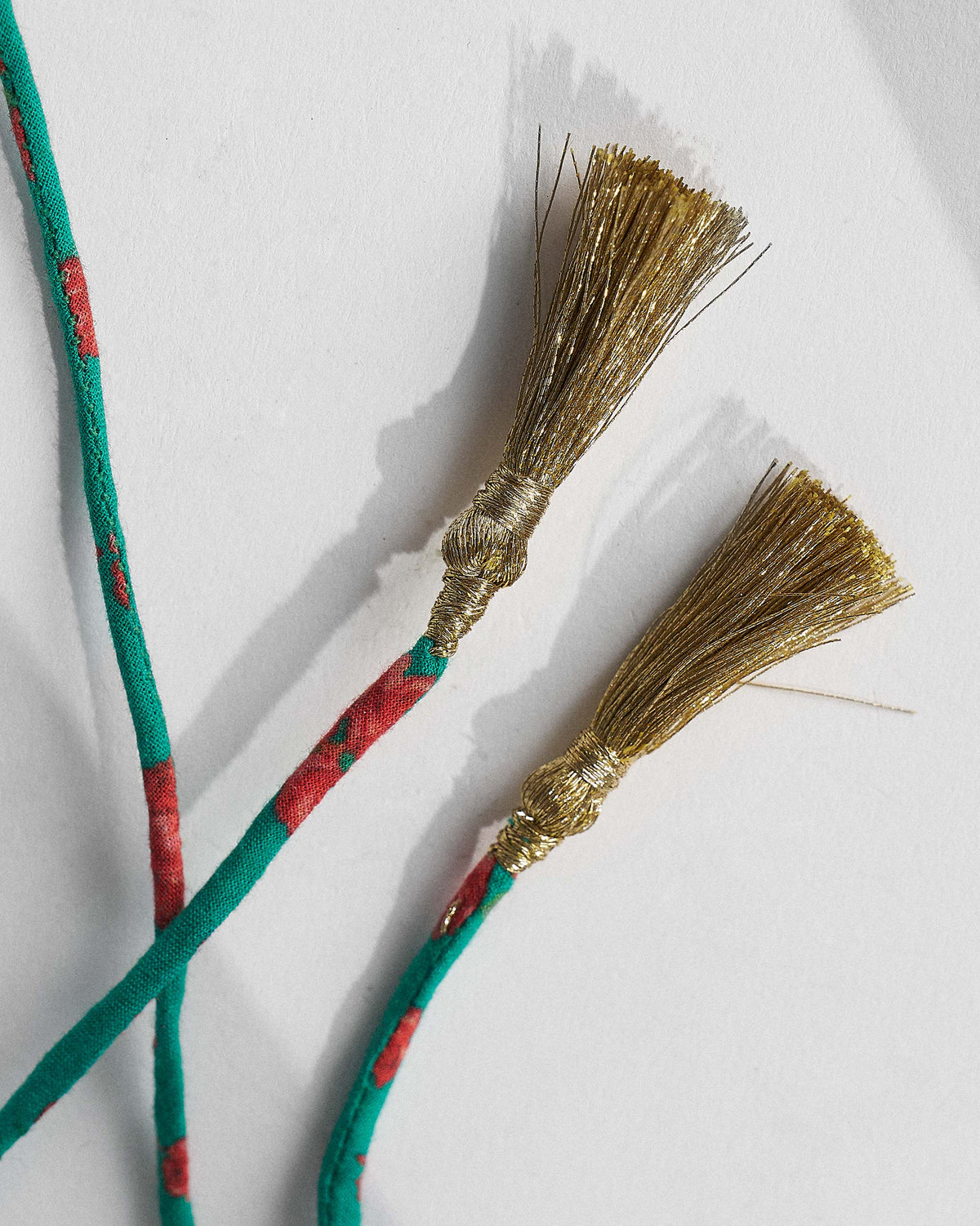 Close-up of gold tassels on the teal cord of a Panch Circle necklace.
