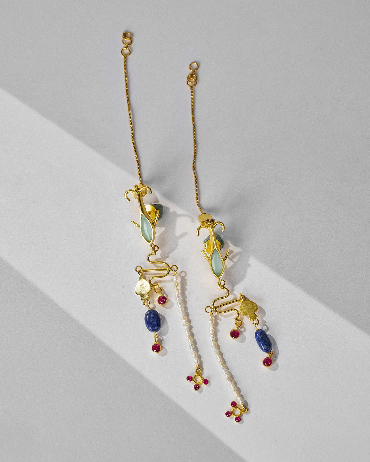 Pair of long gold Indus danglers with stones and pearls laid flat.