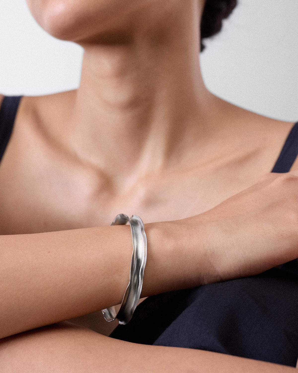 Thin silver Batur bangle worn as a wavy cuff on a wrist.