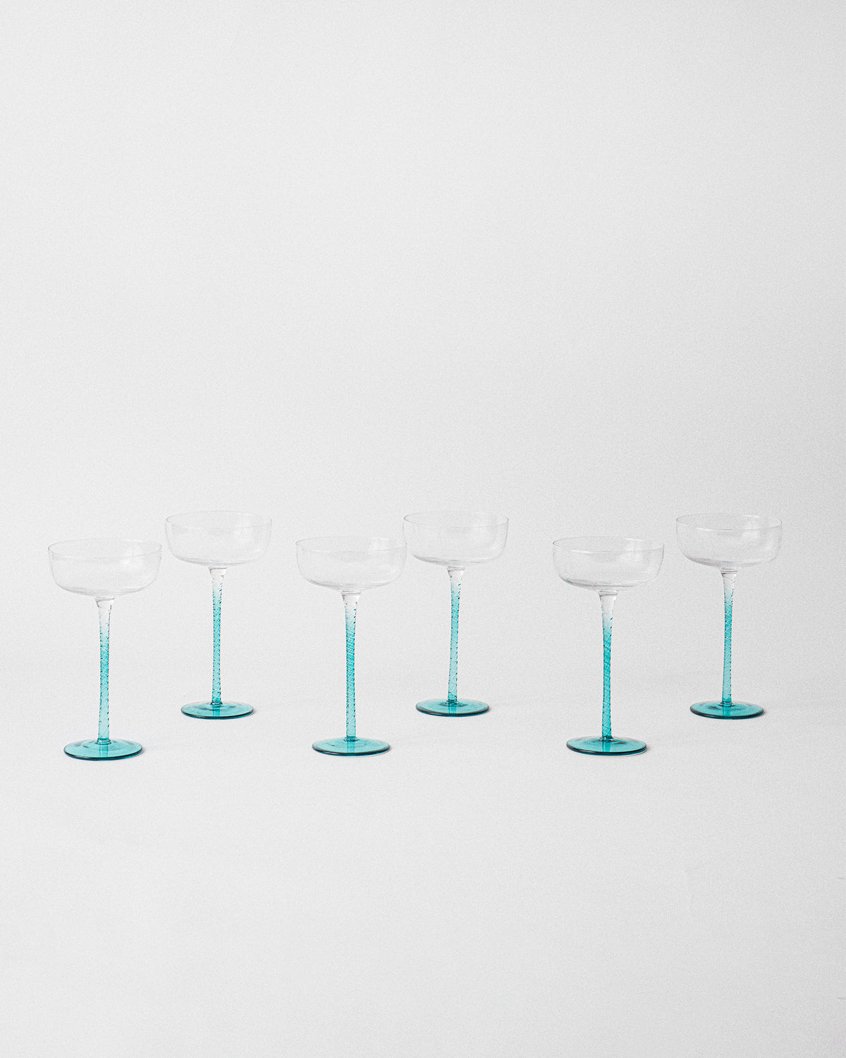 Six Lumen cocktail glasses with teal stems arranged in staggered rows.