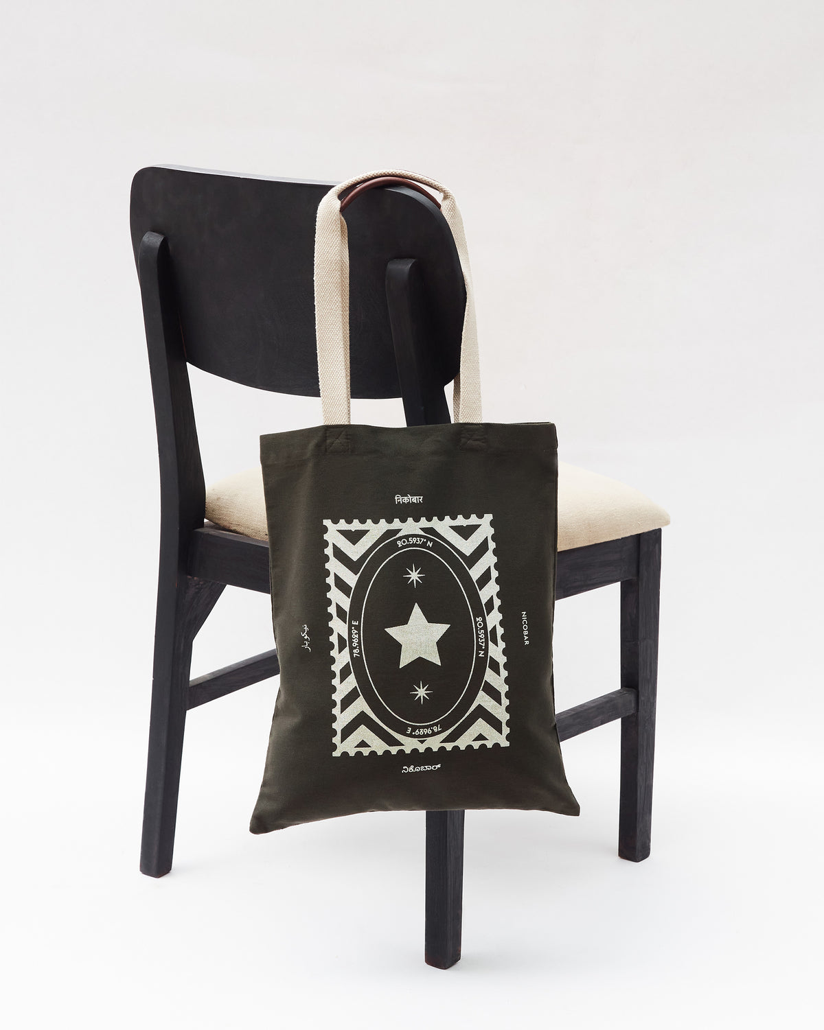 Charcoal Decade Tote with a silver stamp print hung on a wooden chair.