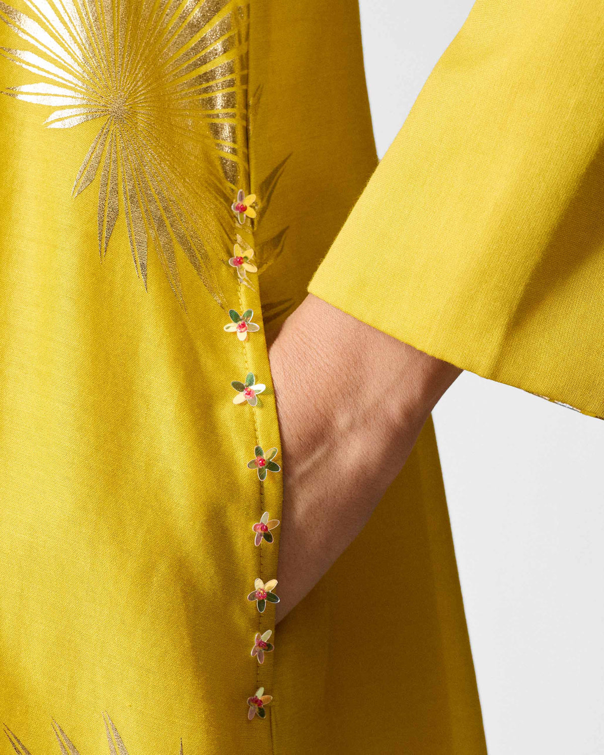 Close-up of a chartreuse kurta pocket with gold palm print and sequin trim.