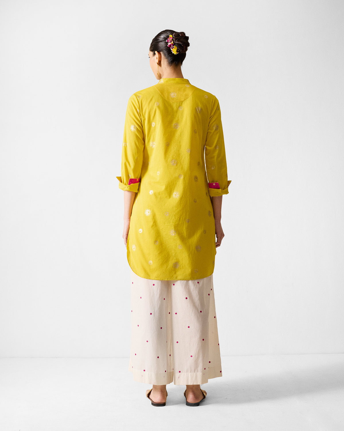 Back of a chartreuse mid-length kurta with gold motifs and a curved hem.