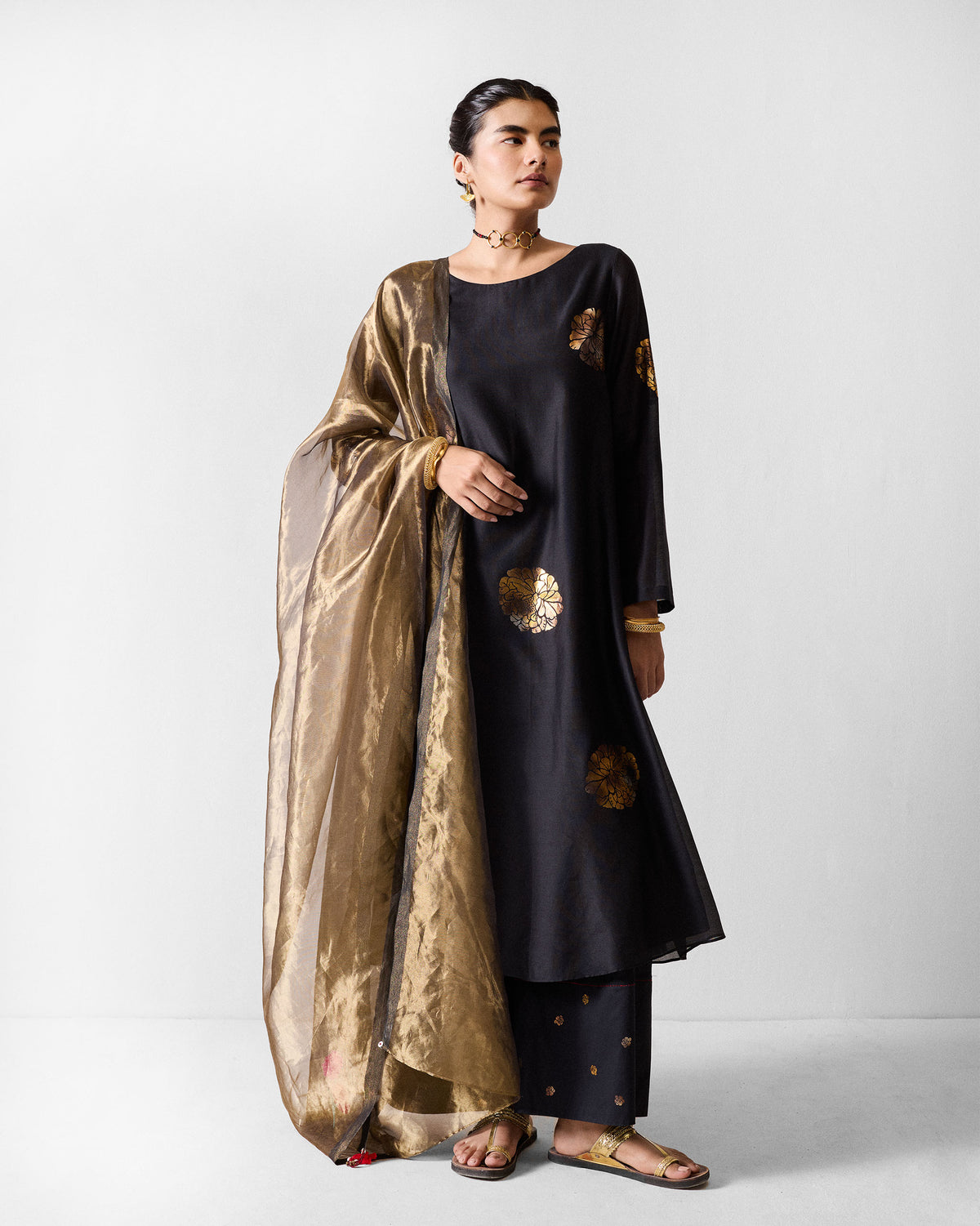 Person wearing a black and gold boat-neck kurta with a metallic gold dupatta.