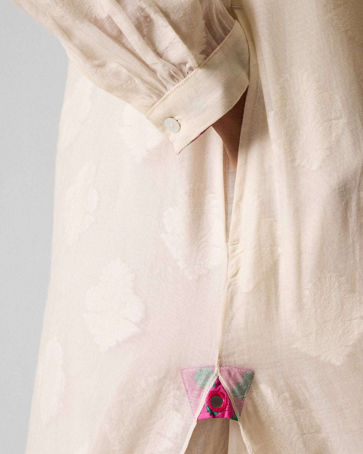 Close-up of pink mirror work at the side slit of an ivory kurta.