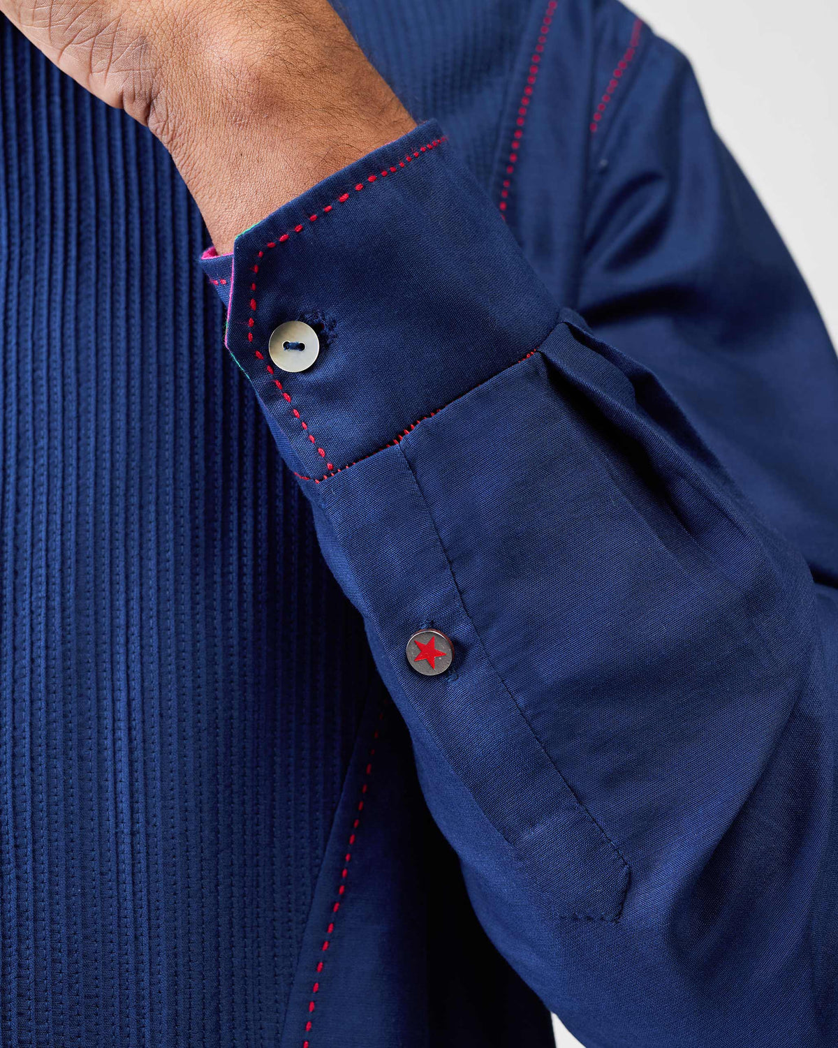Close-up of a navy Talha kurta cuff with red stitching and star button.