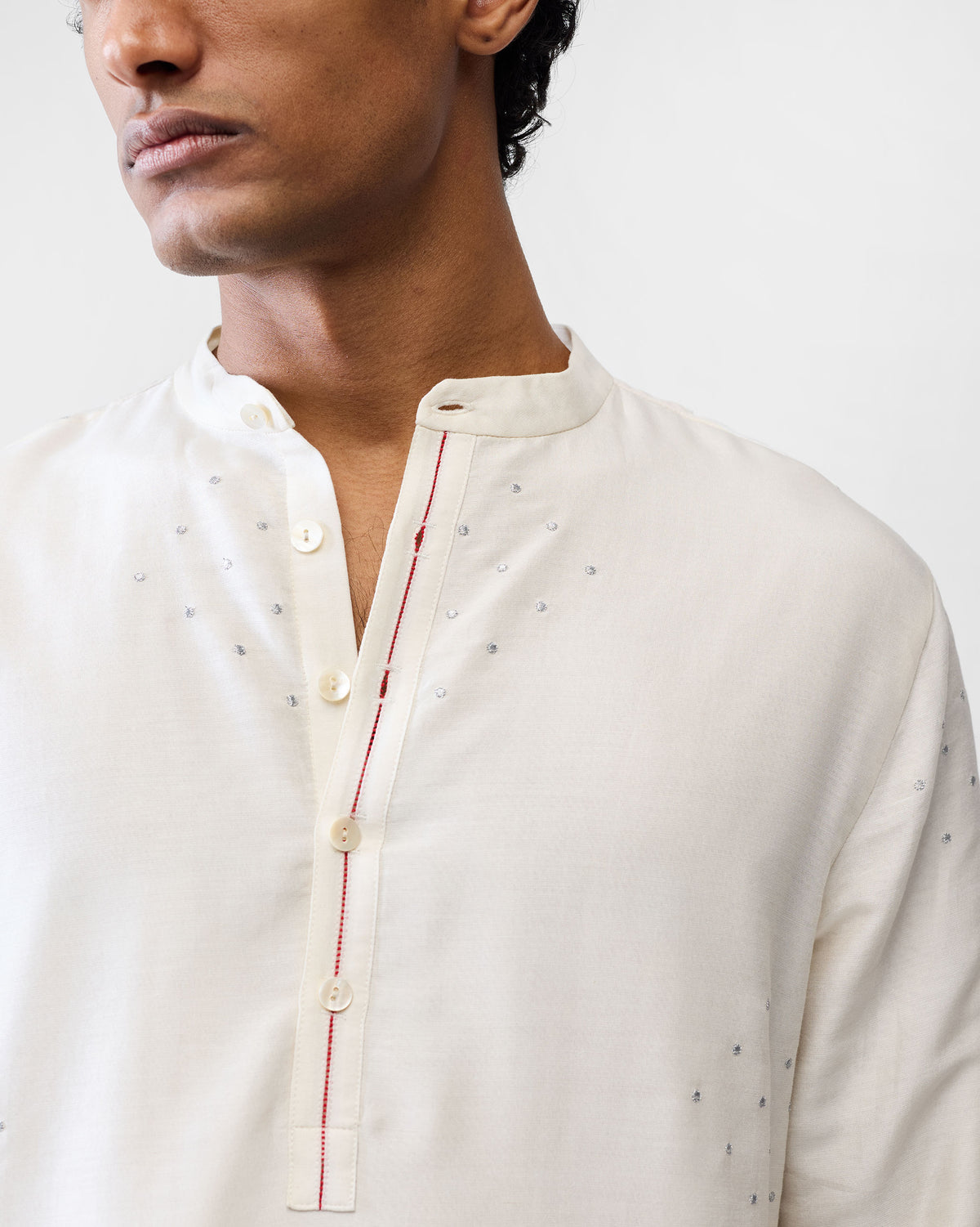 Close-up of an ivory astral kurta placket with red stitching and silver hearts.
