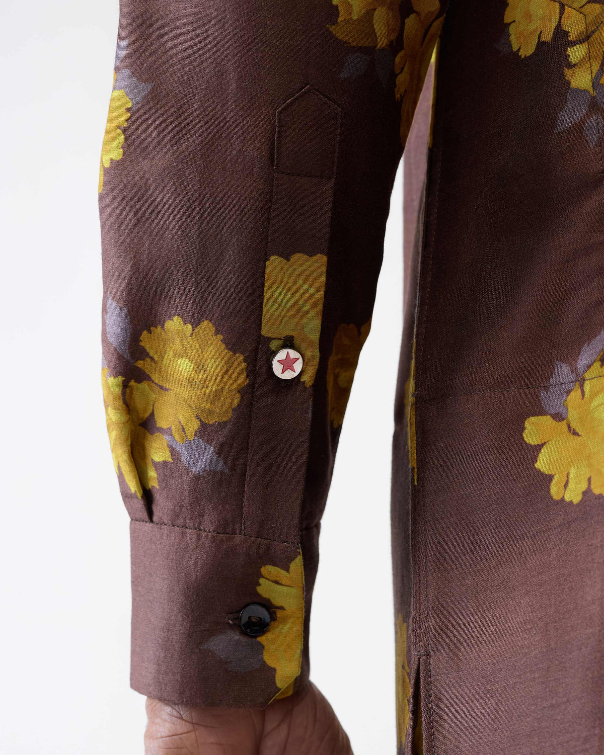 Close-up of a brown Astral kurta sleeve with yellow flowers and a red star button.