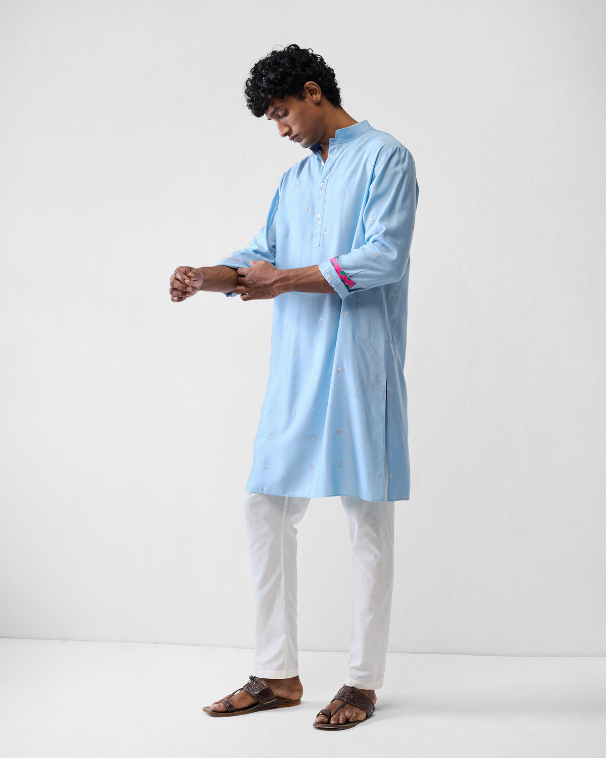 Person rolling a light blue Rey kurta sleeve to show pink floral lining.