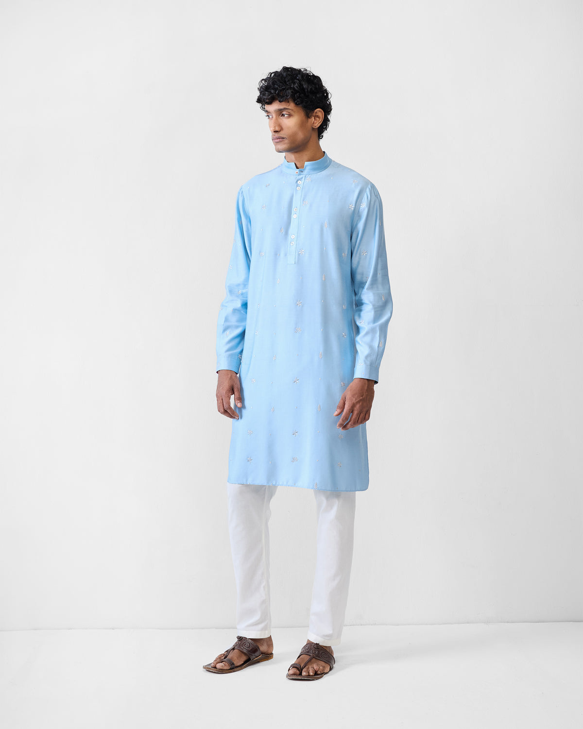Full-length view of a light blue embroidered Rey kurta with white trousers.