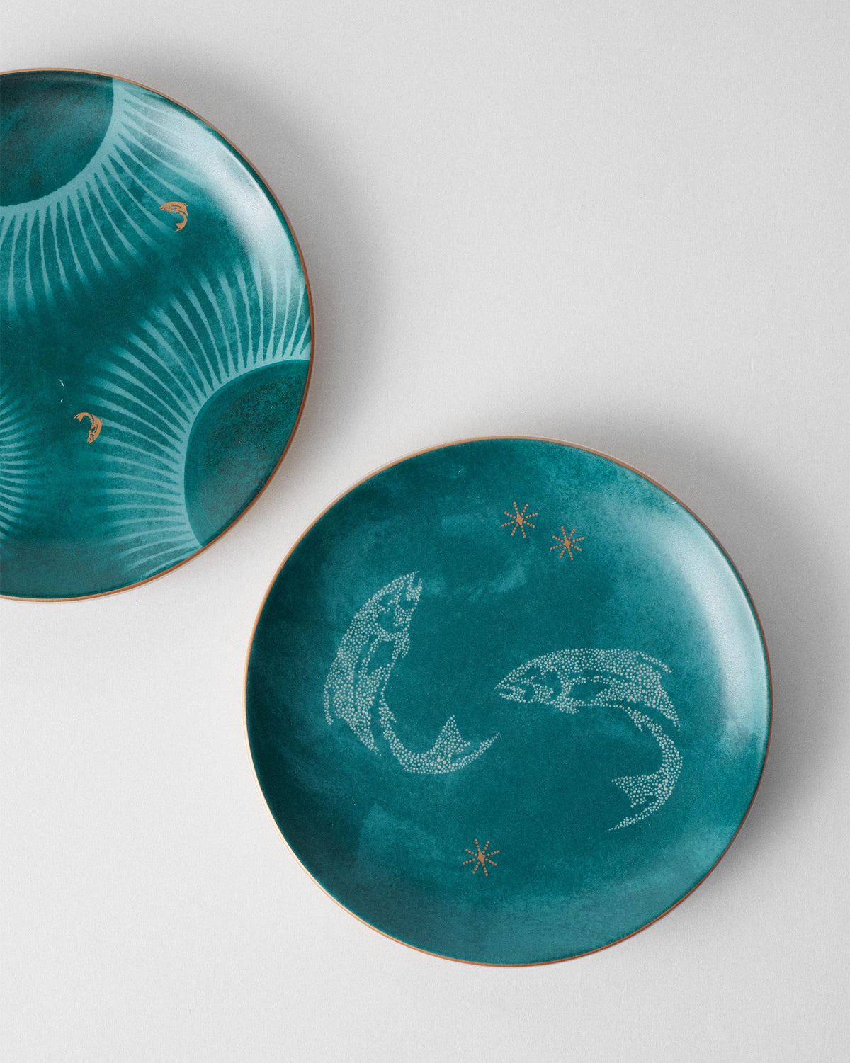 Teal Caden plate with two stippled white fish and gold star accents.