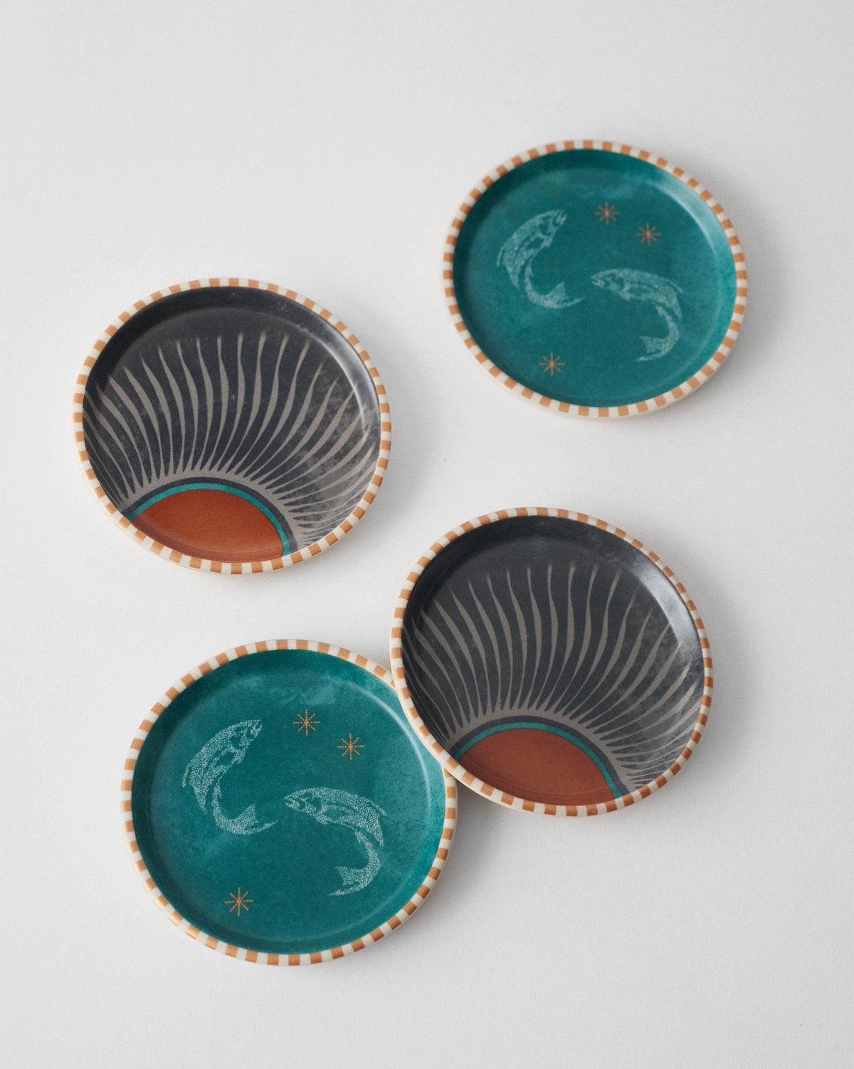 Four Aluna coasters laid out showing teal fish and charcoal sunburst prints.