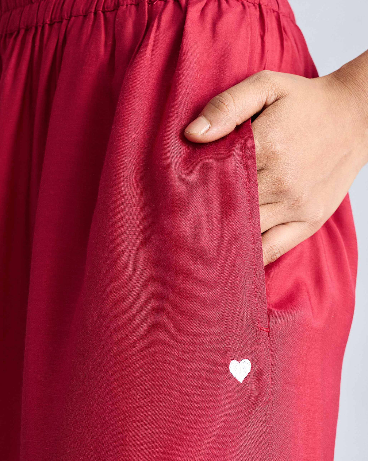 Close-up of red Classic Pyjama pants with a side pocket and white heart embroidery.