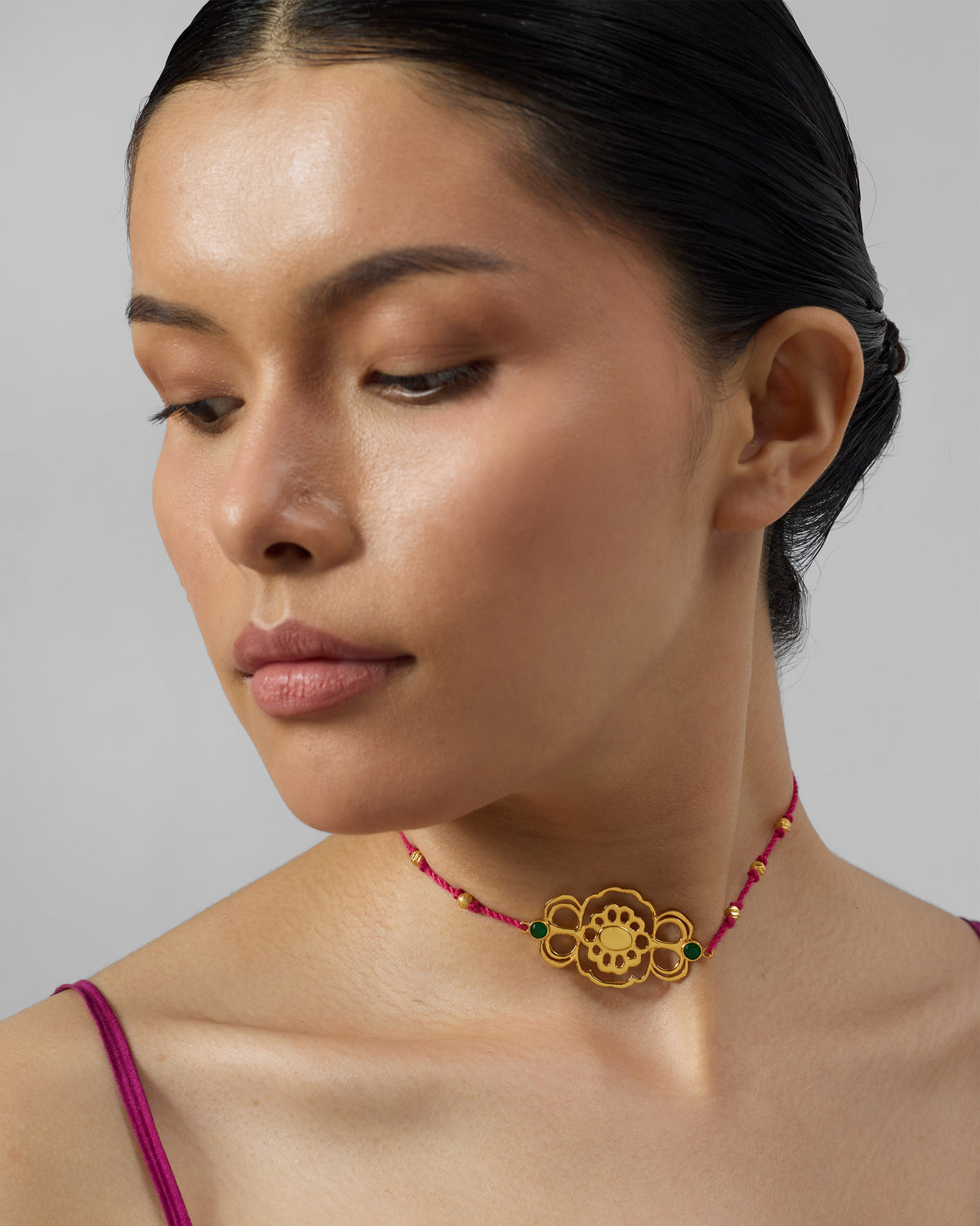 Person wearing a gold titli choker on a magenta cord.