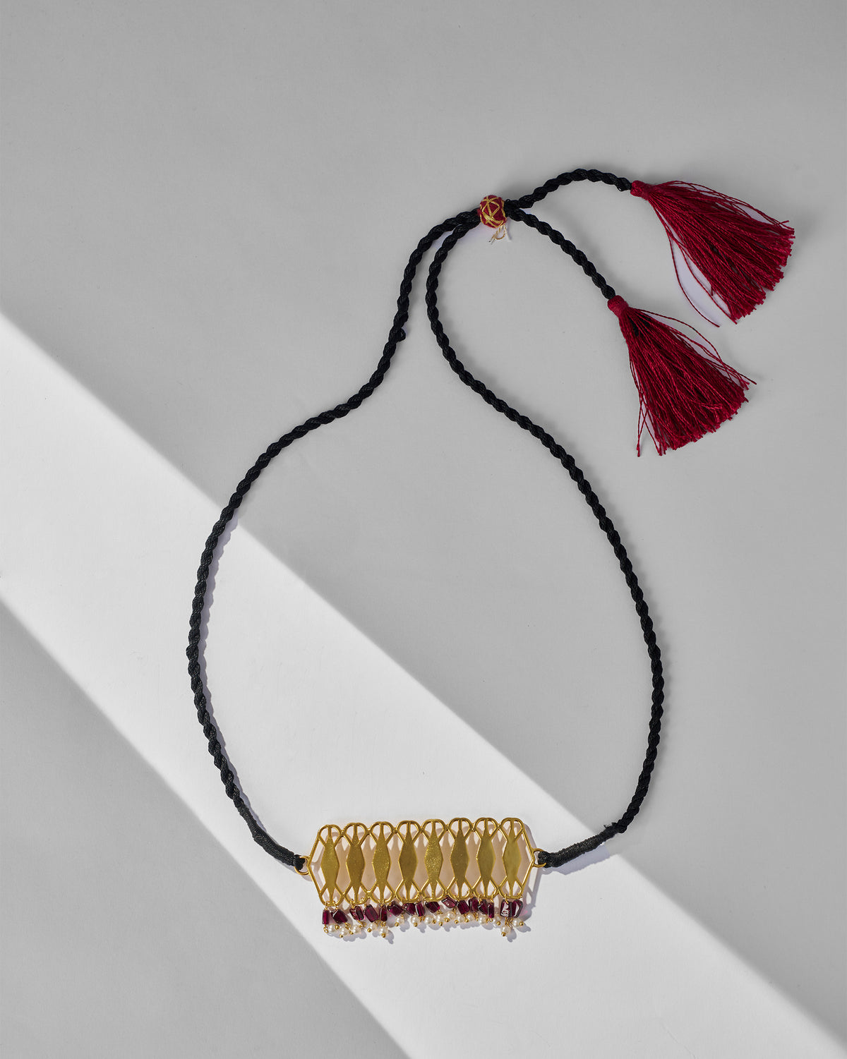 Gold Barfi choker with lattice plate, garnet fringe, and maroon tassels.