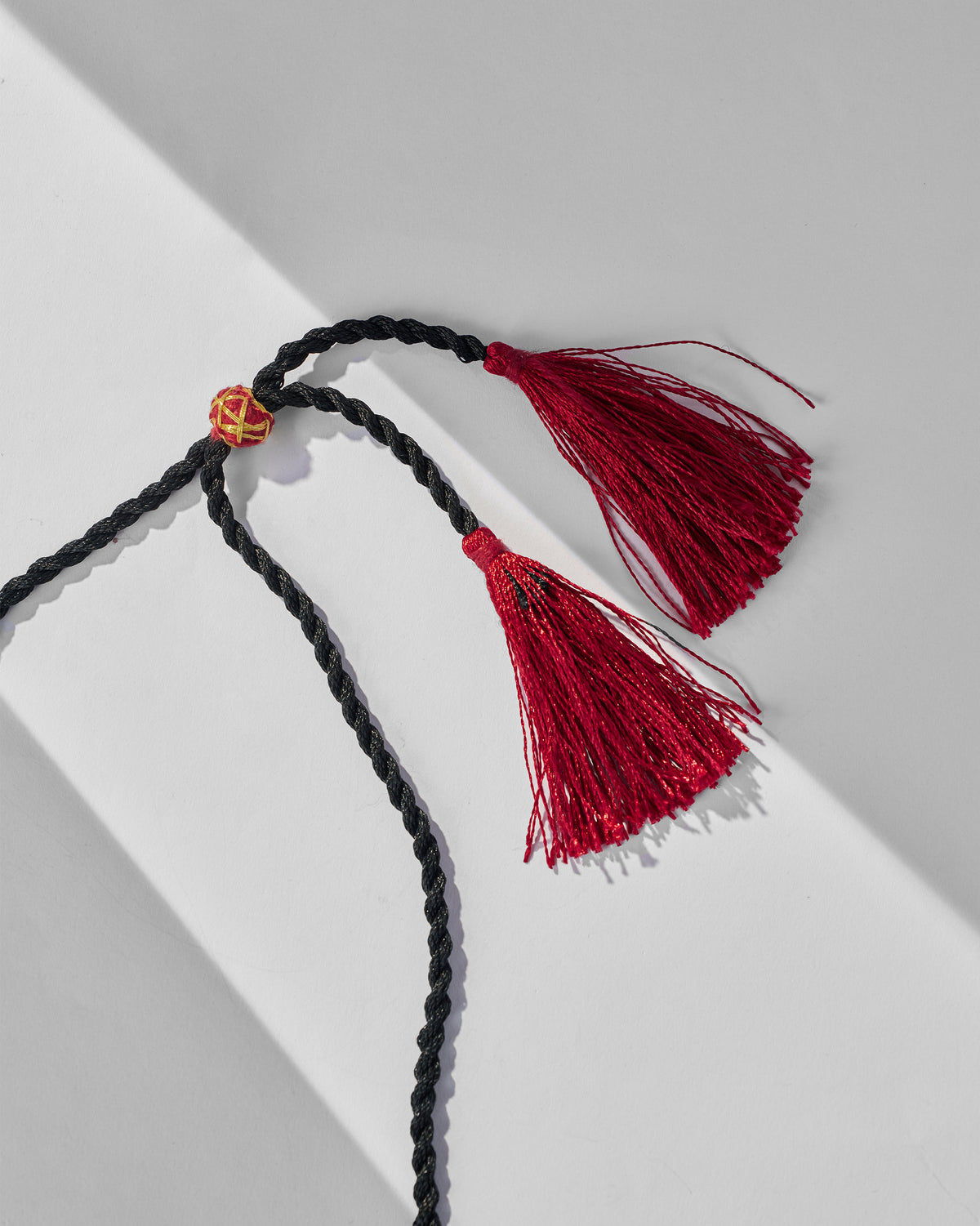 Close-up of the black cord and maroon tassels on the Barfi choker.