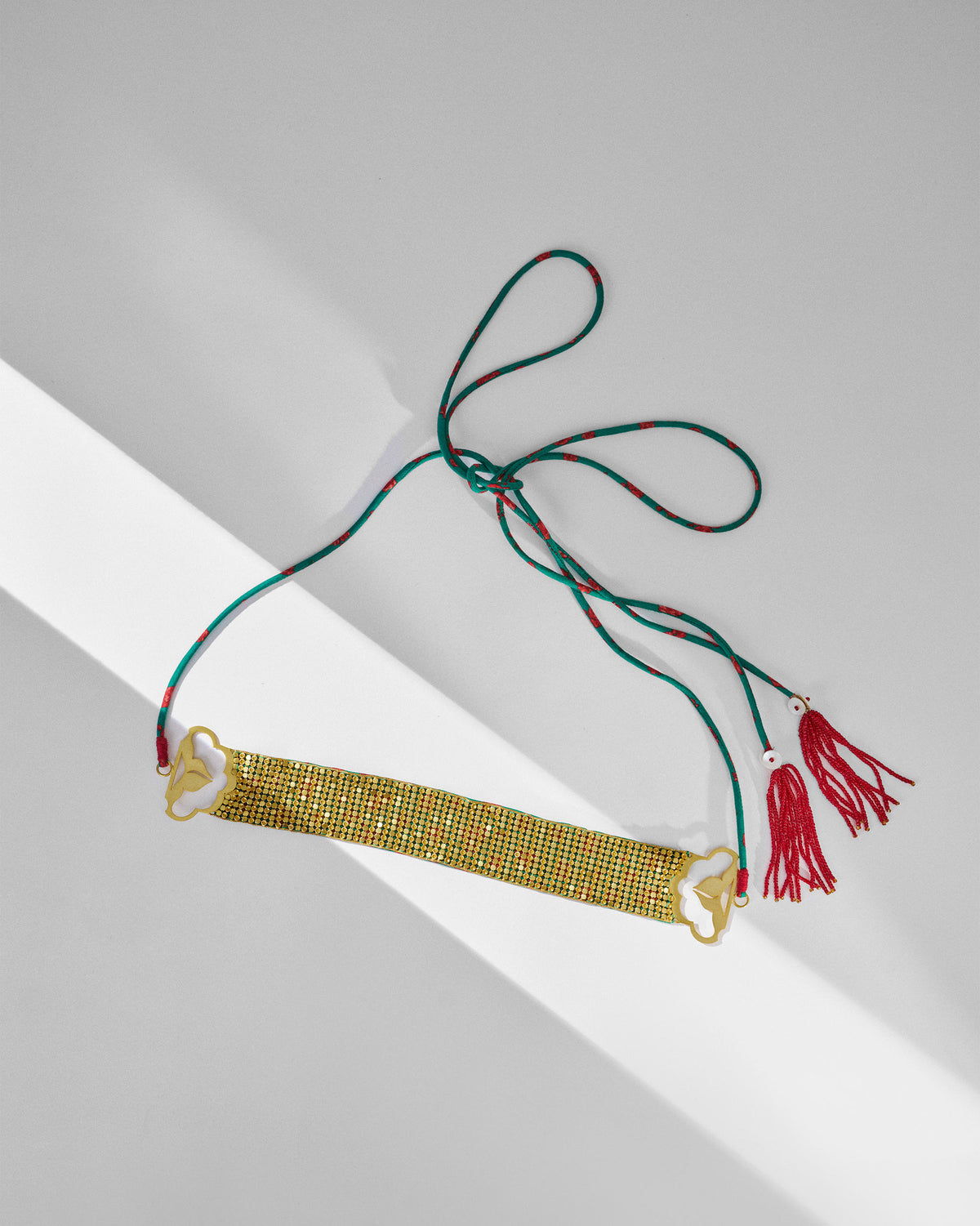 Gold Chain Mail necklace laid flat with green ties and red tassels.