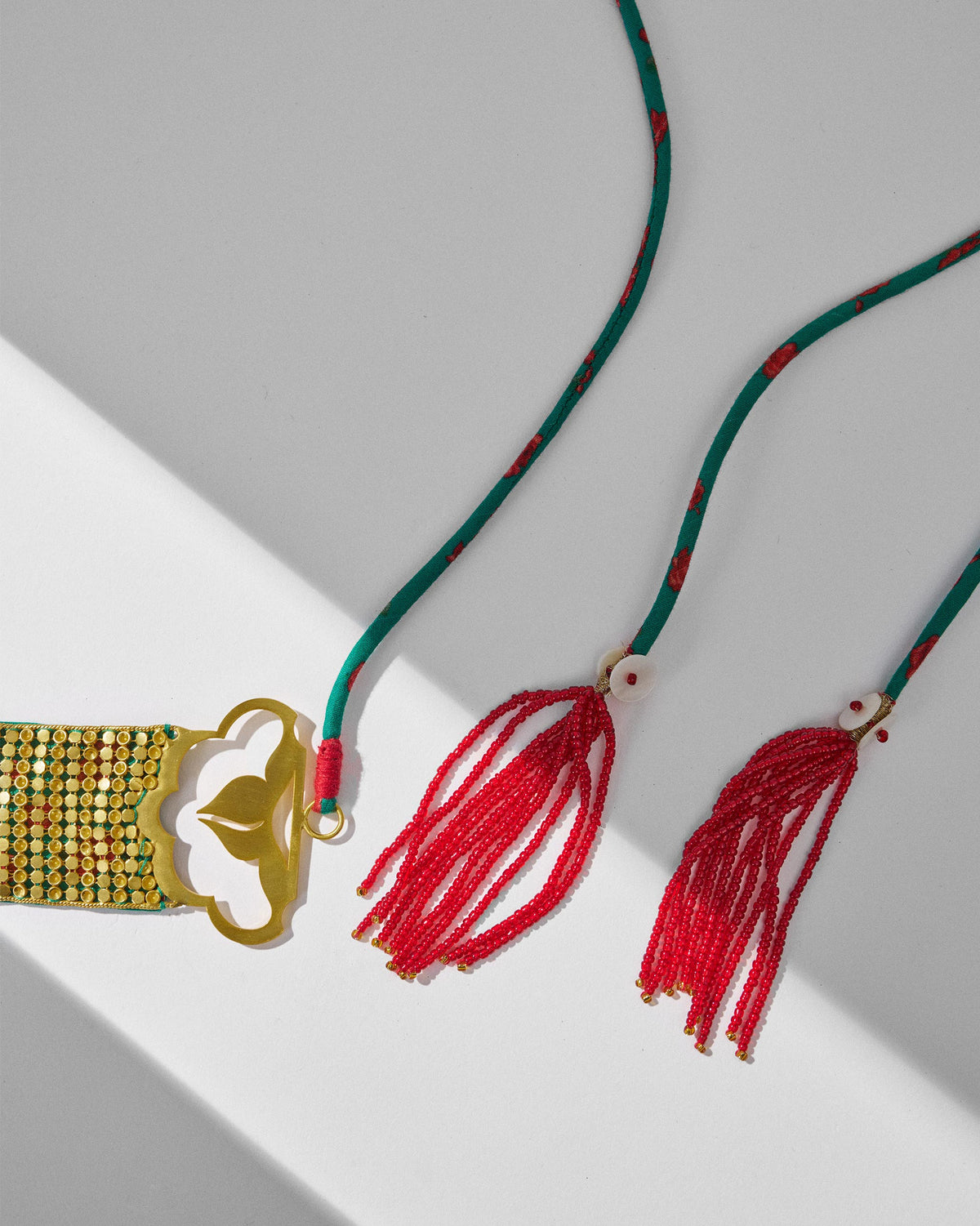 Close-up of Chain Mail necklace endcap with green cord and red tassels.
