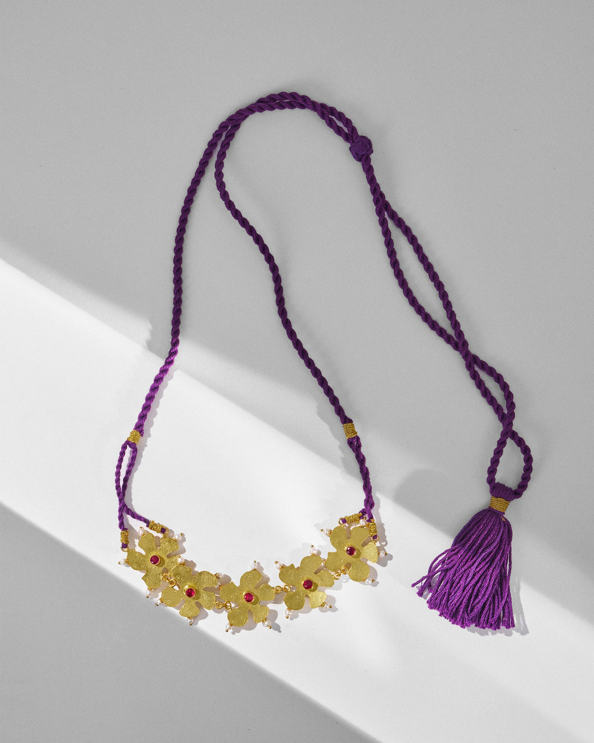 Gold phool haar necklace with floral motifs laid flat on a purple cord.