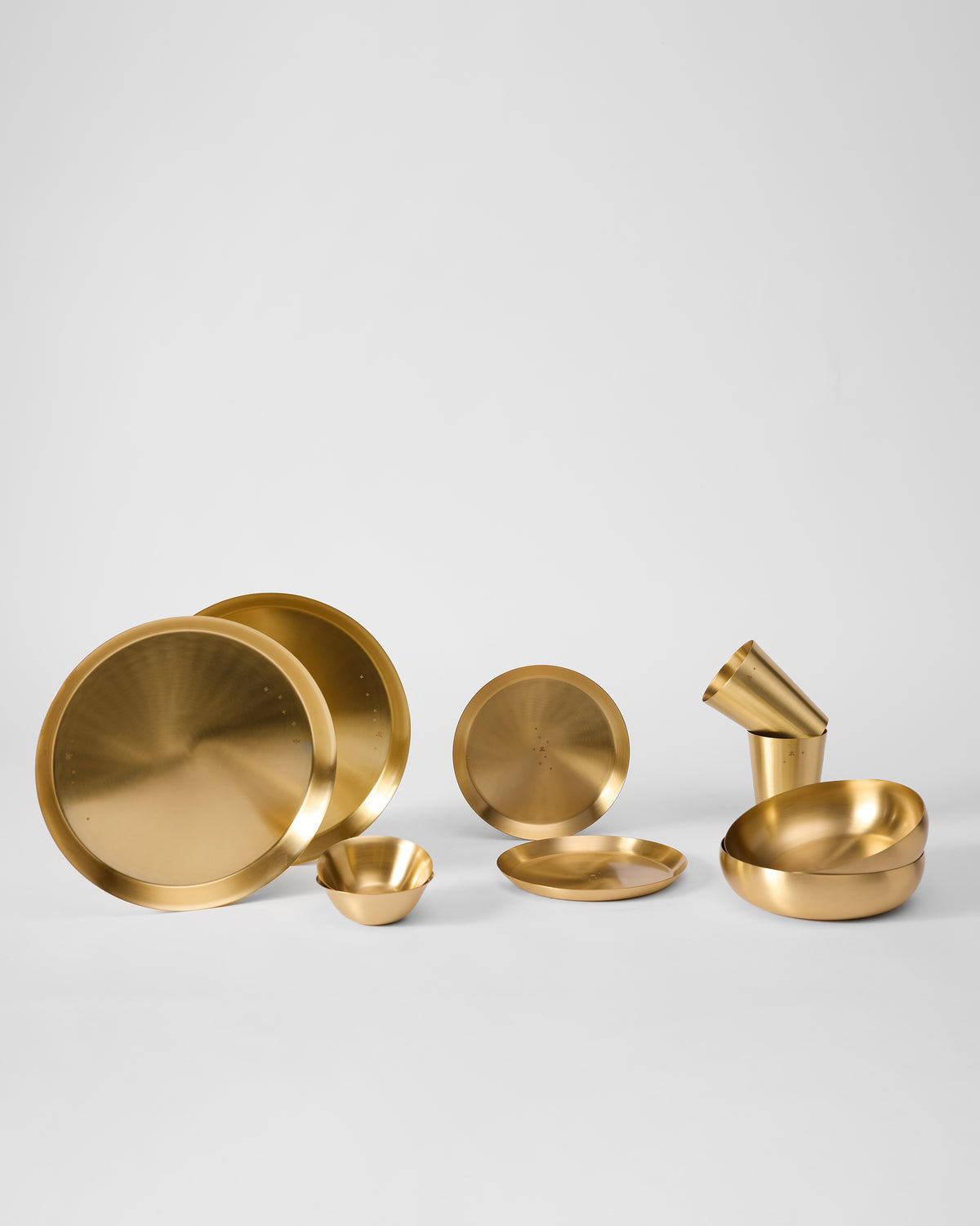 Gold plates, bowls and cups from the Madhu Dinner Gift Set laid out in a row.