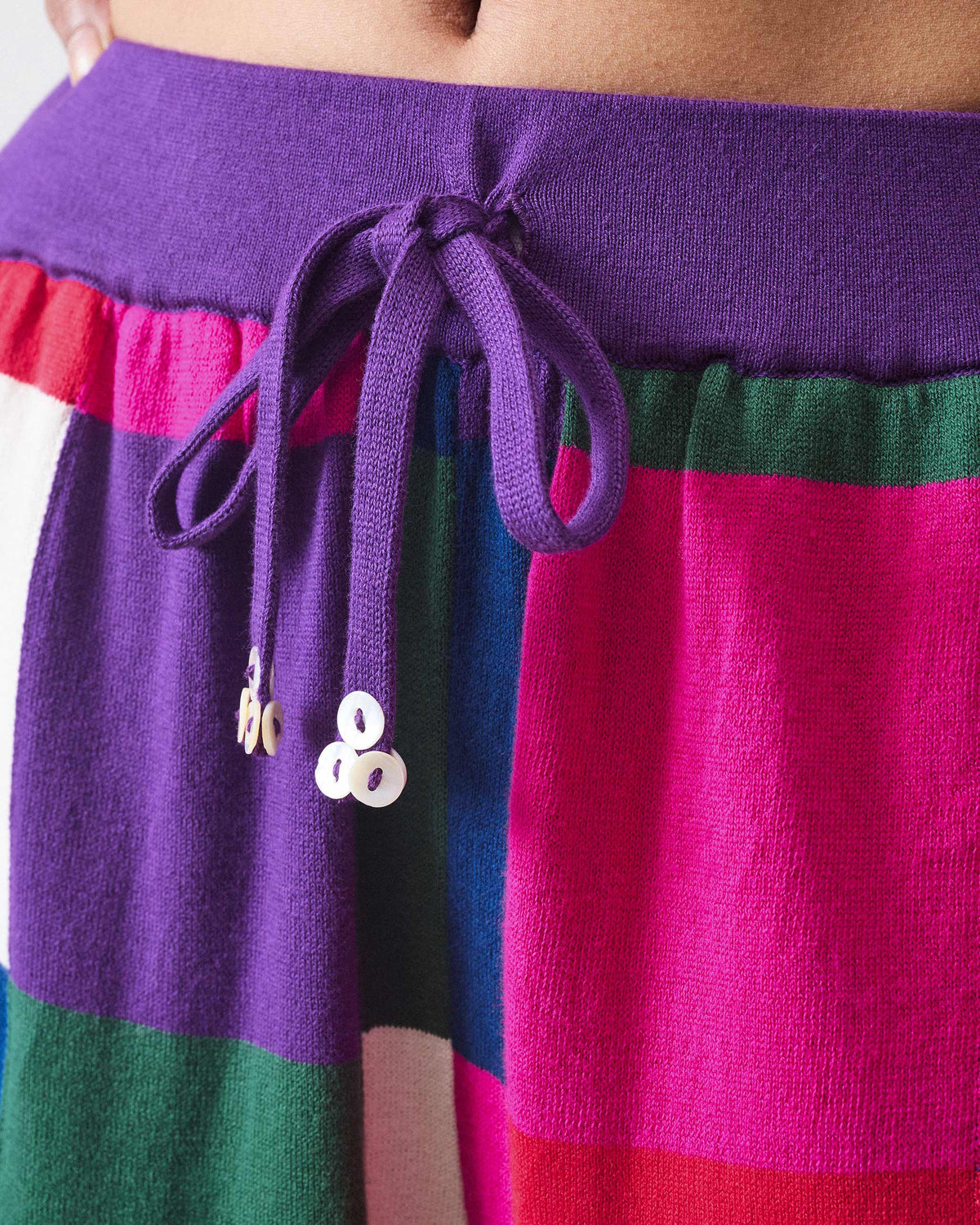 Close-up of a purple drawstring waistband on multicolour knit trousers.