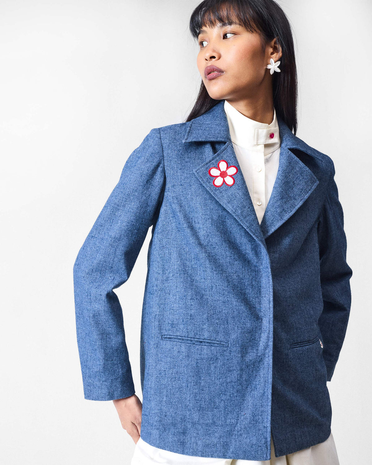 Person wearing a dust blue Trace Jacket with a flower motif on the lapel.