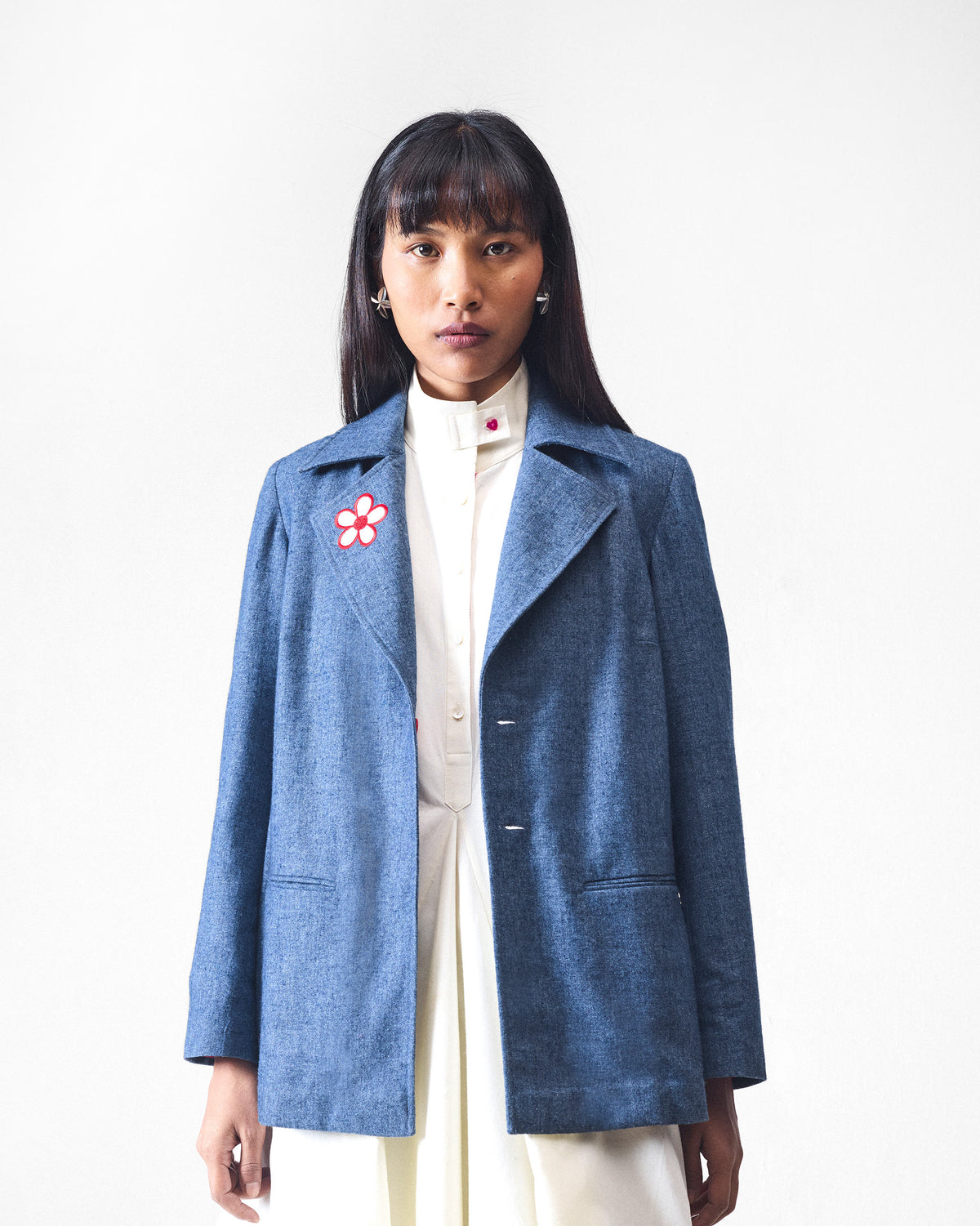 Person wearing an open dust blue Trace Jacket with a chest flower motif.