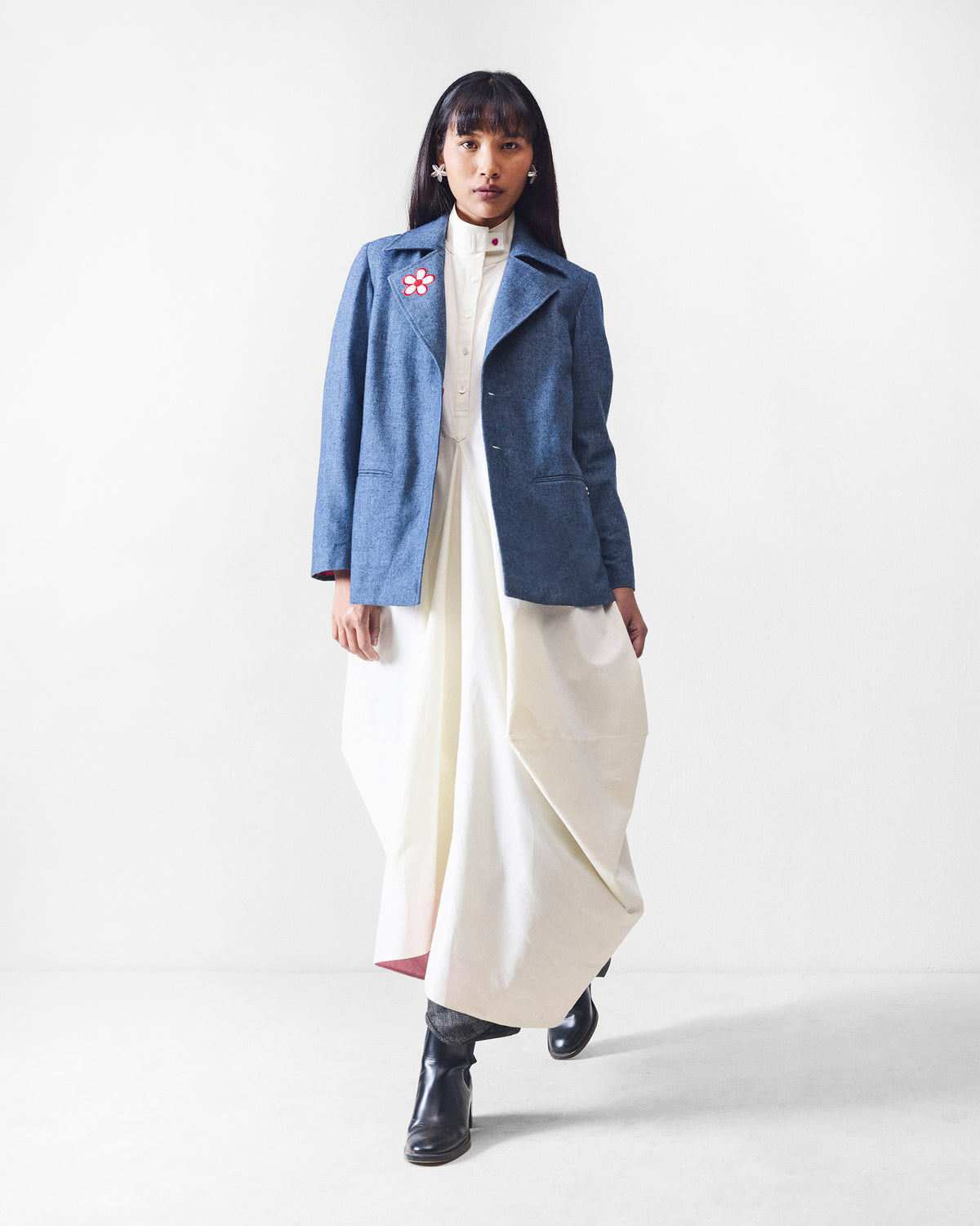 Person wearing a dust blue Trace Jacket with a flower motif over a white dress.