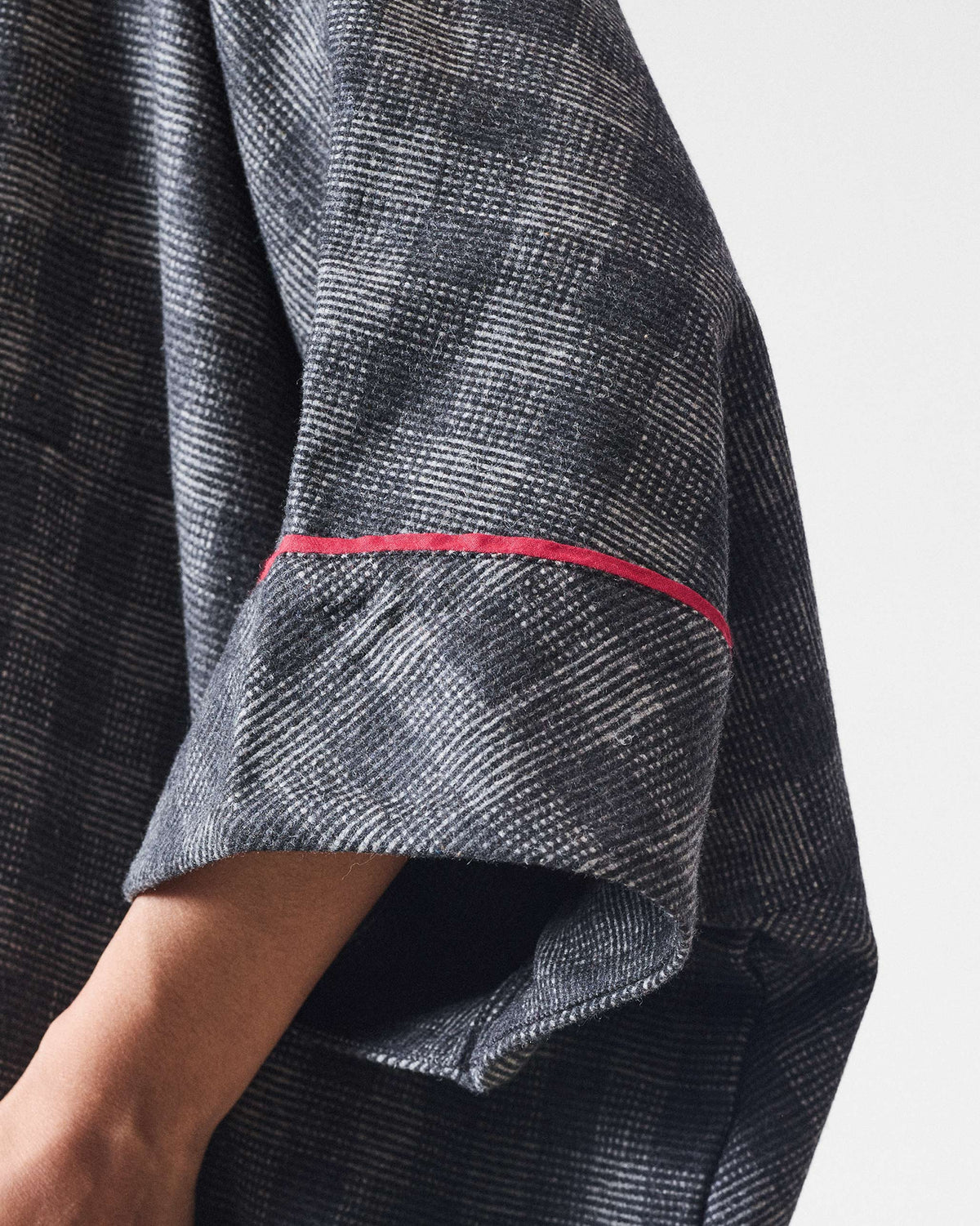 Close-up of Fable Top sleeve in charcoal check with a red accent line.