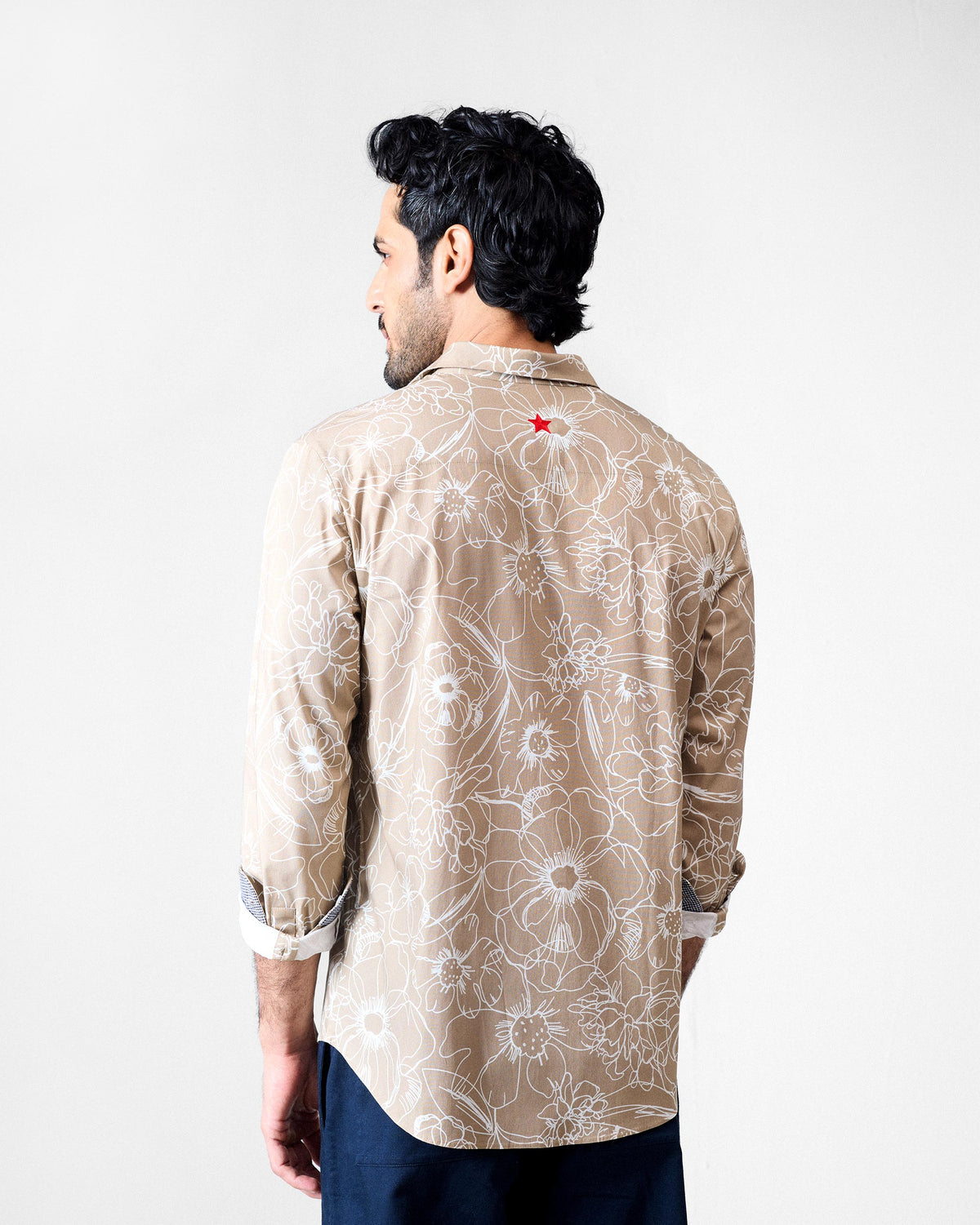 Back of a light brown Hakuna Shirt with a white floral print and red star.