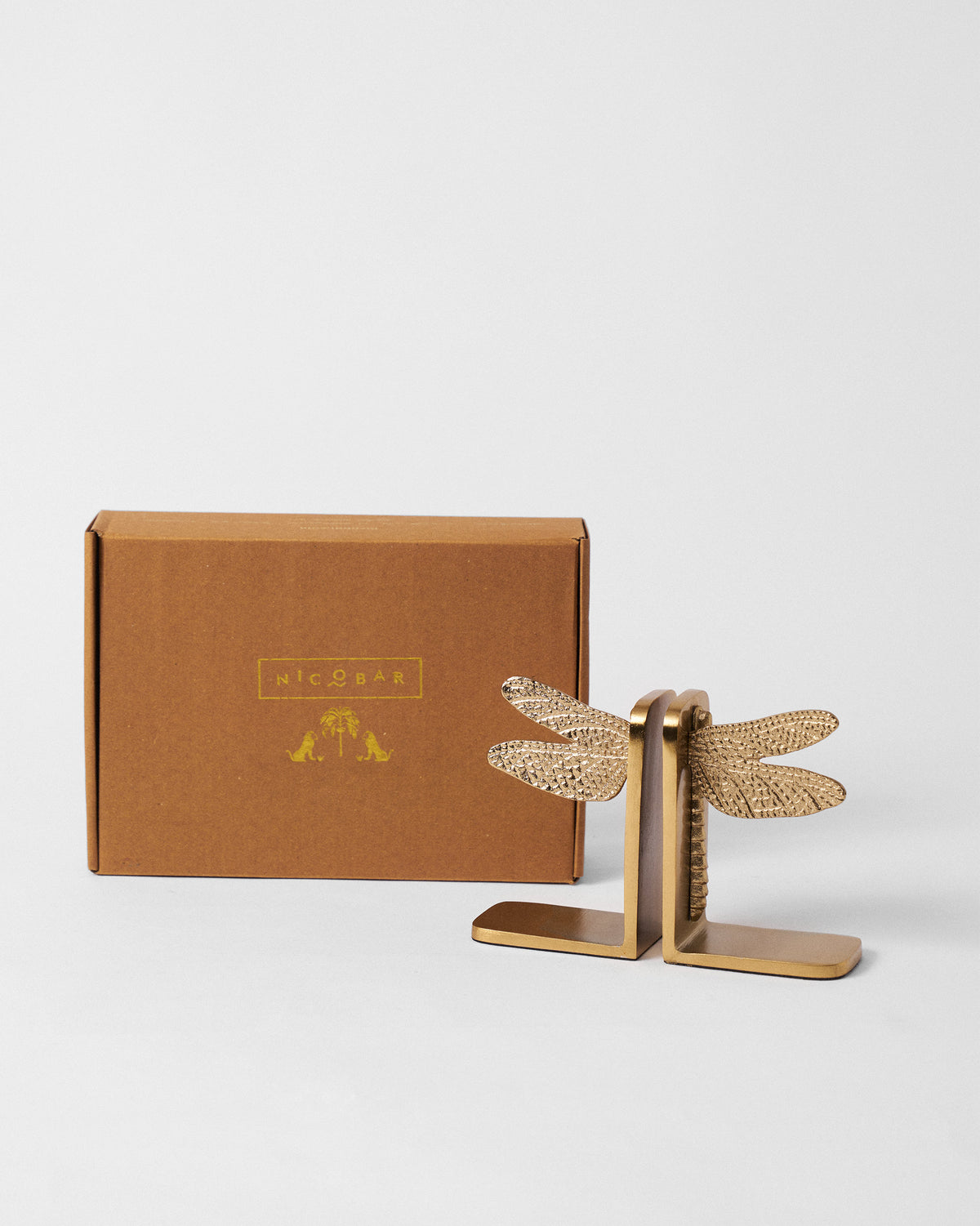 Gold dragonfly bookends standing in front of a Nicobar gift box.
