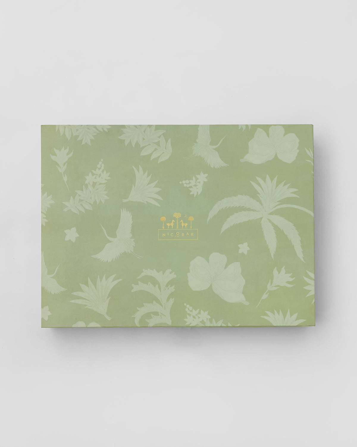 Sage green Nicobar gift box with tropical leaf and crane print.