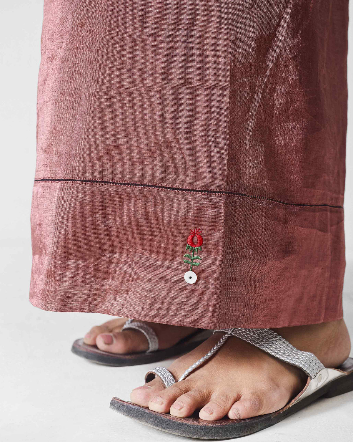 Close-up of pink Charisma pants hem with red anar embroidery and an ivory button.